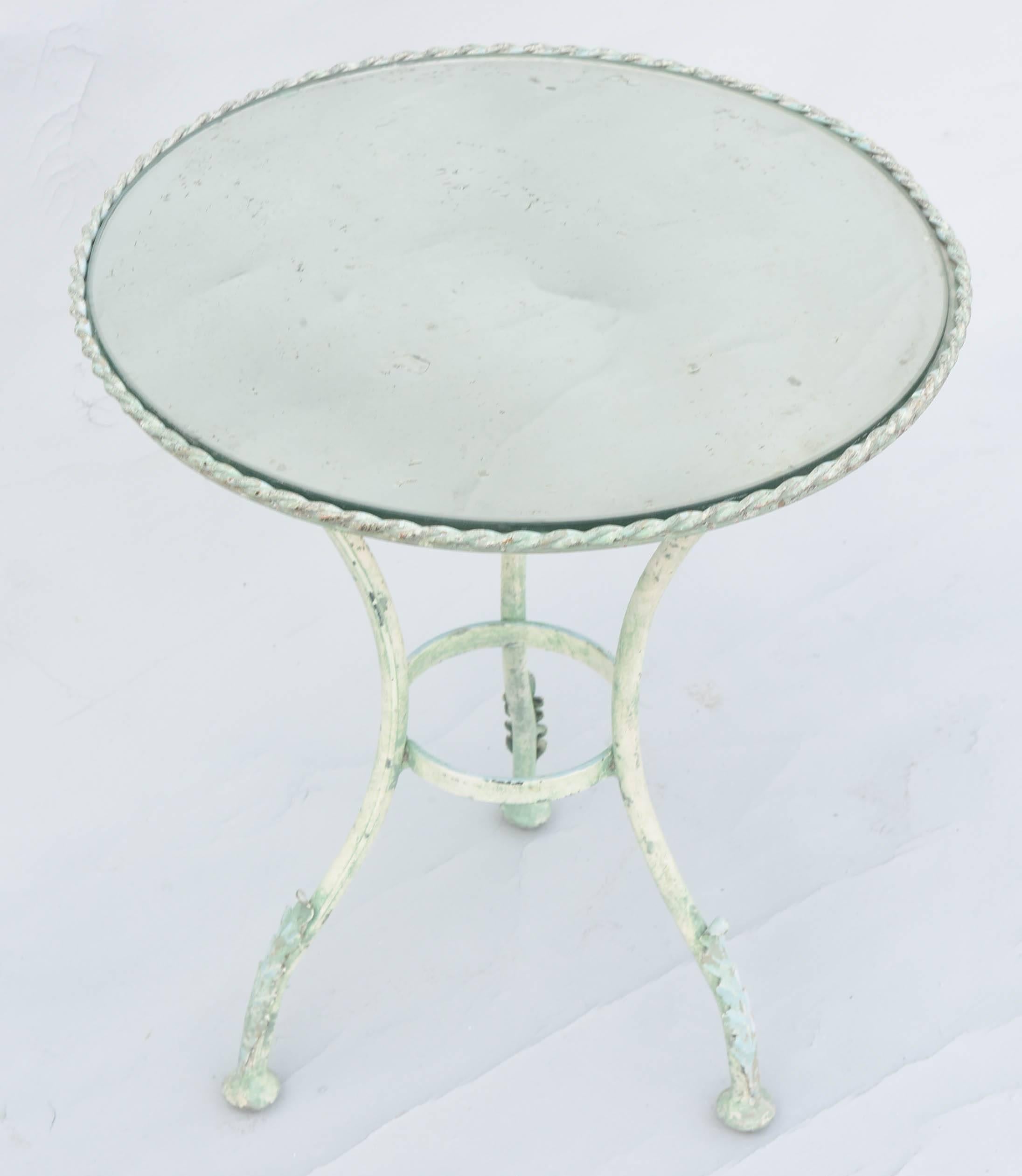 Side table, of metal with verdigris finish, having a round top of distressed mirror, in twisted border, raised on three splayed legs, joined by circular stretcher, ending in foliate decorated feet. 