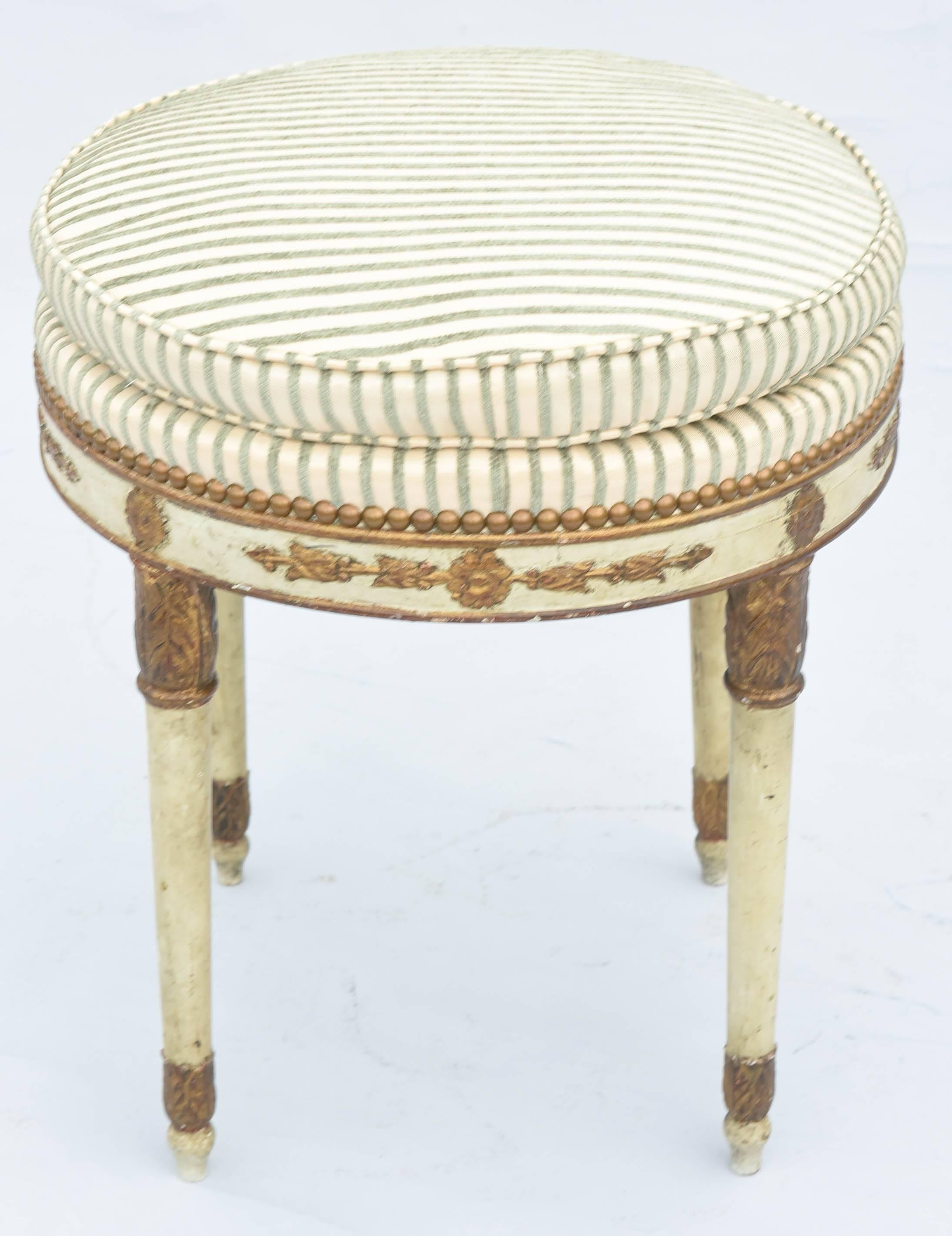 Stool, having a round boxed seat, of striped chenille, finished with nailheads, on painted and parcel gilt base, its apron decorated by rosettes and acanthus, raised on foliate-headed, round, tapering legs, ending in acanthine, touipe feet.

Stock