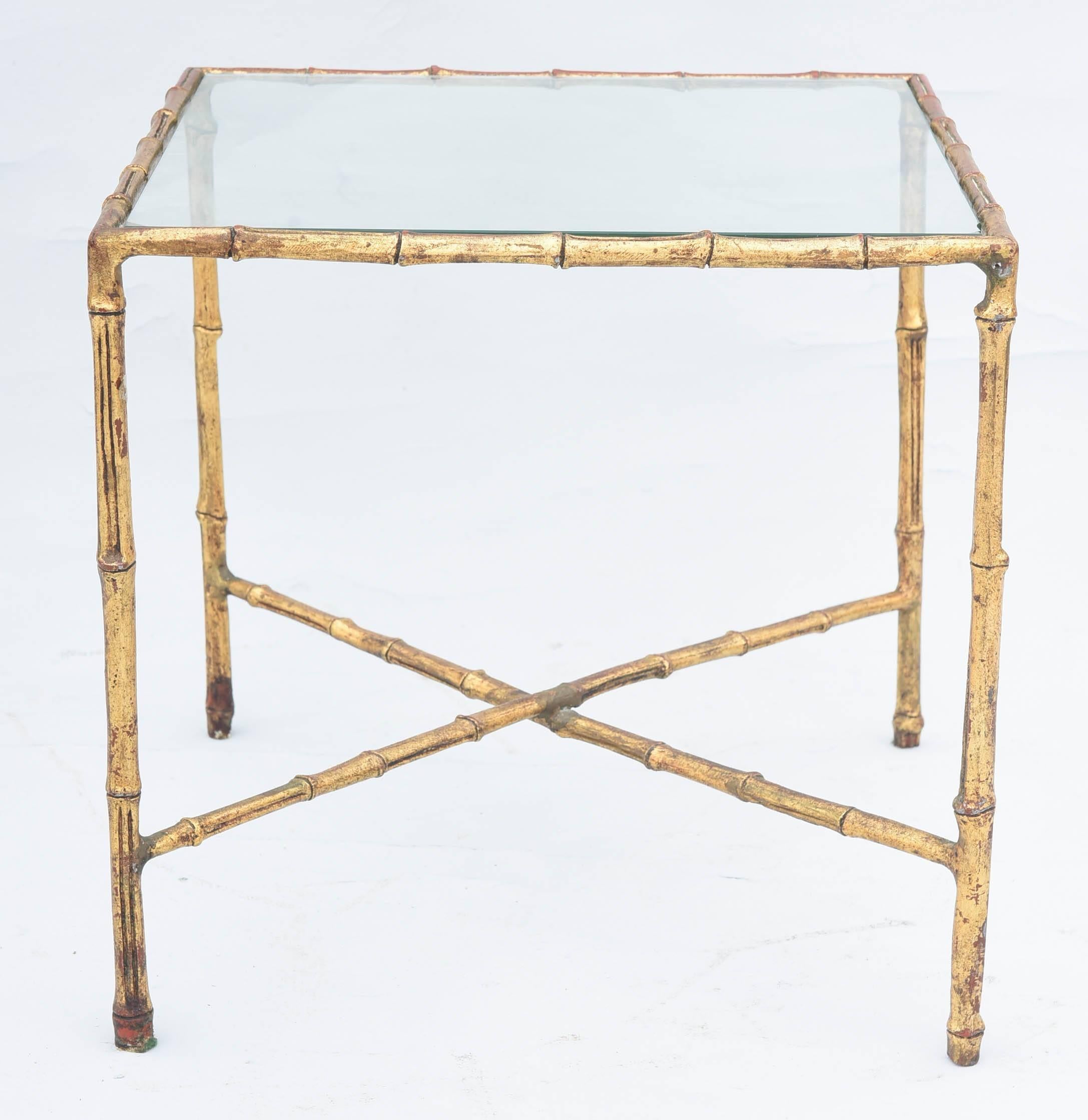 Side table, of gilded iron, its faux bamboo frame, holding a top of clear glass, raised on straight legs, joined by X-stretcher. 