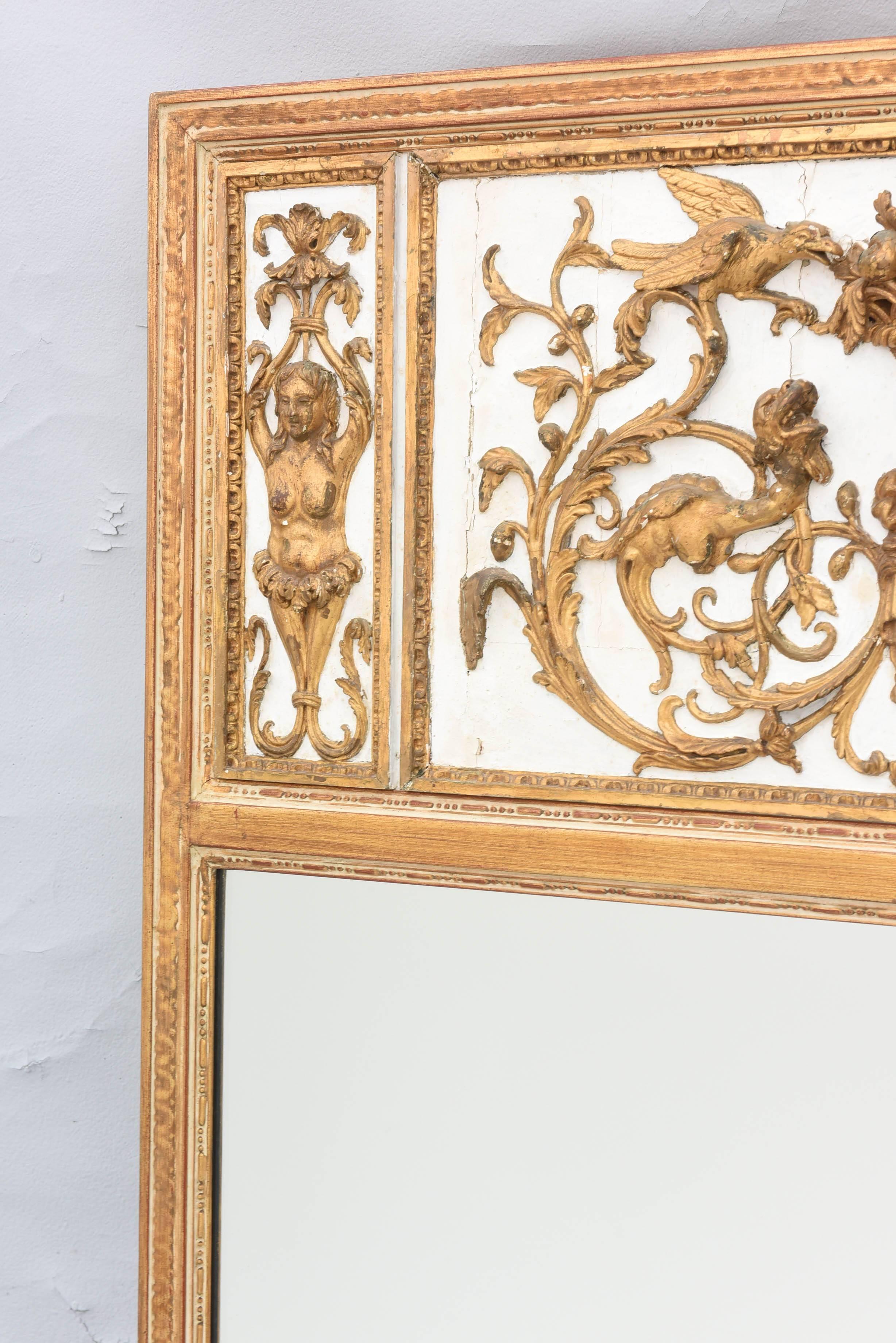 Miroir Trumeau, son cadre rectangulaire sculpté de godrons et de perles, surmonté d'un panneau du XVIIIe siècle, décoré de sculptures classiques élaborées et dorées ; le panneau central est sculpté d'un masque sous un panier rempli de fruits,