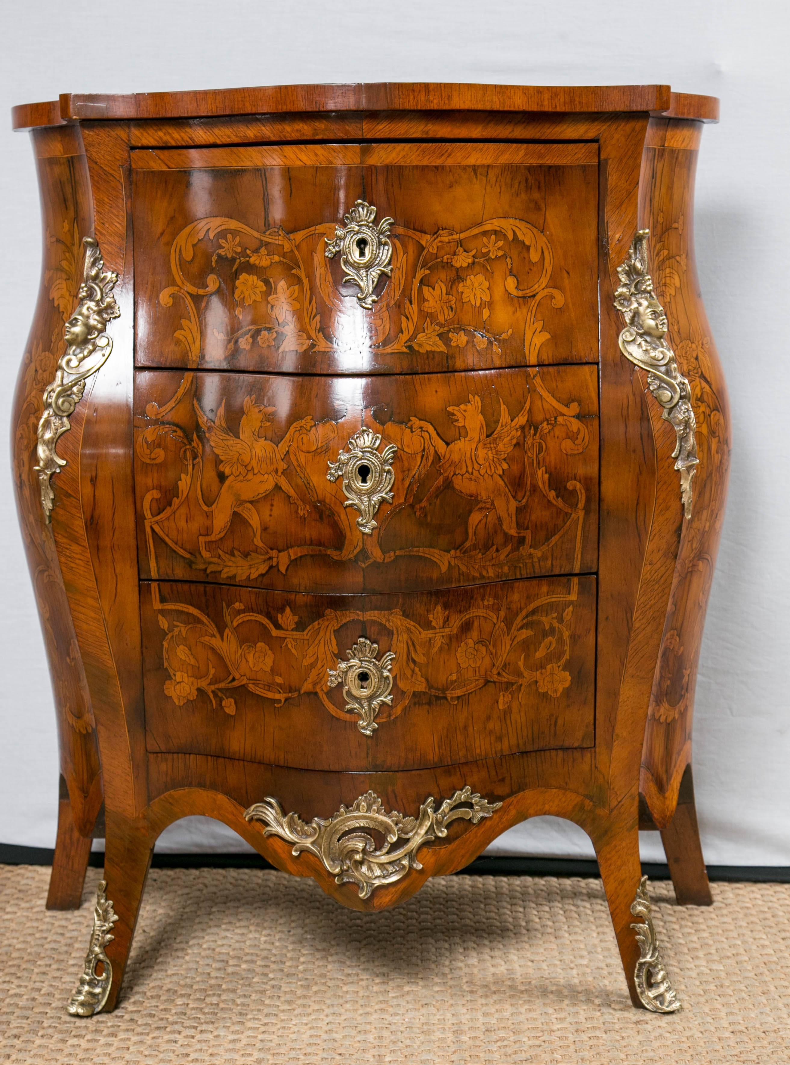 Dating from the late 19th century, this bombe style commode has gilt bronze mounts and marquetry inlays on both the front, sides and top. It has a deep shaped top and deep apron.
 