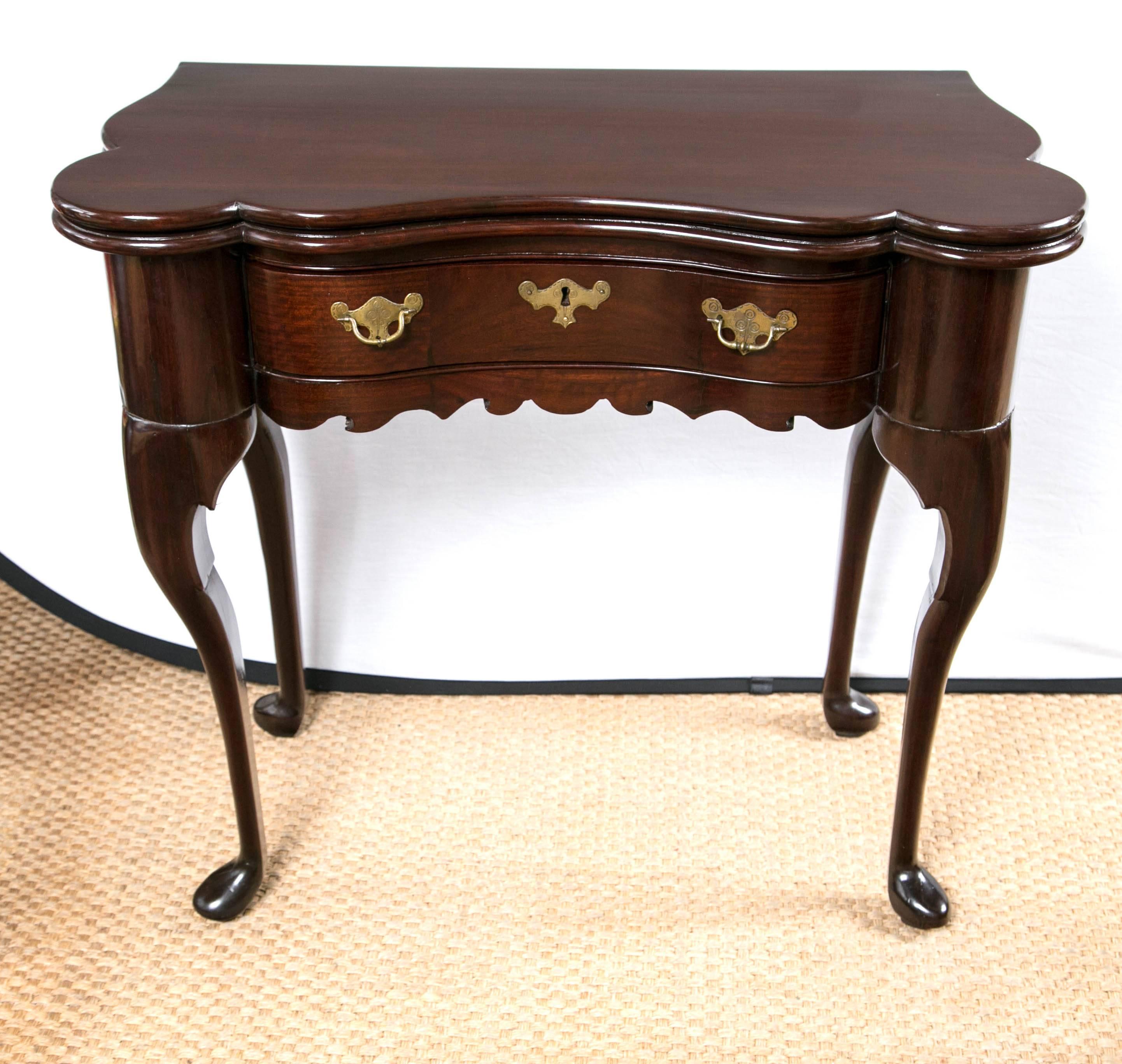 A Fine English game/card table, dating from the 18th century, with a flip-top and lined in green baize. It has deeply rounded corners and concaved front and shaped sides. A single drawer with original pulls and escutcheon. Wave design frieze under