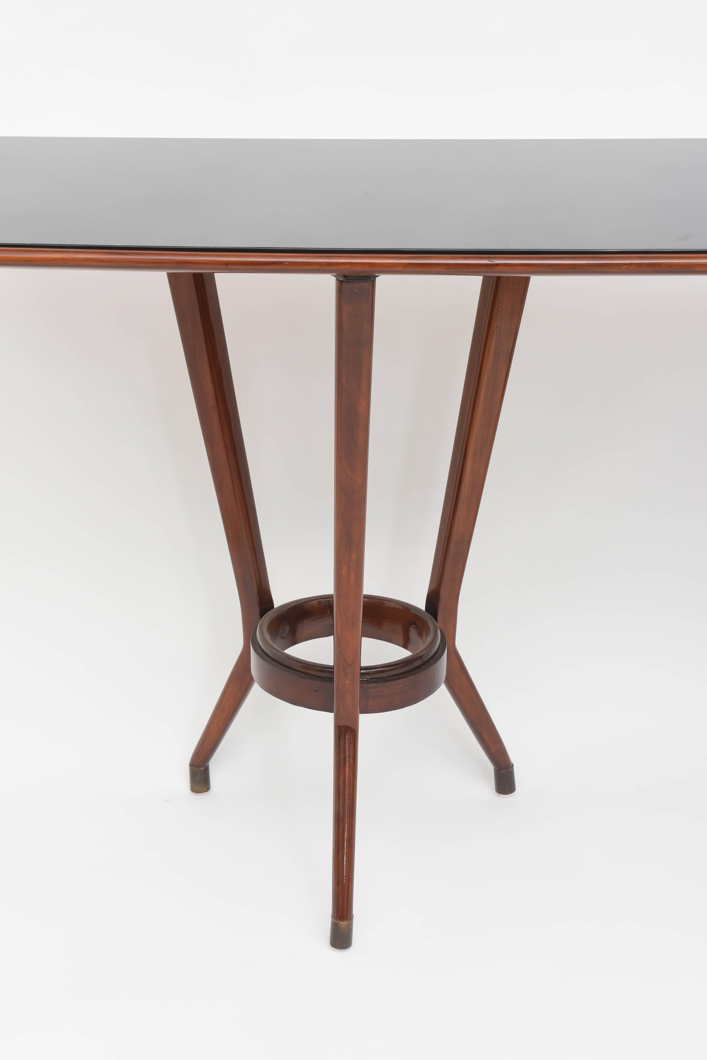 The inset black glass rectangular top with rounded edges with wood trim above two tripartite base supports joined by a ring stretcher,
literature- Guglielmo Ulrich, drawing/rendering of table, p 200.