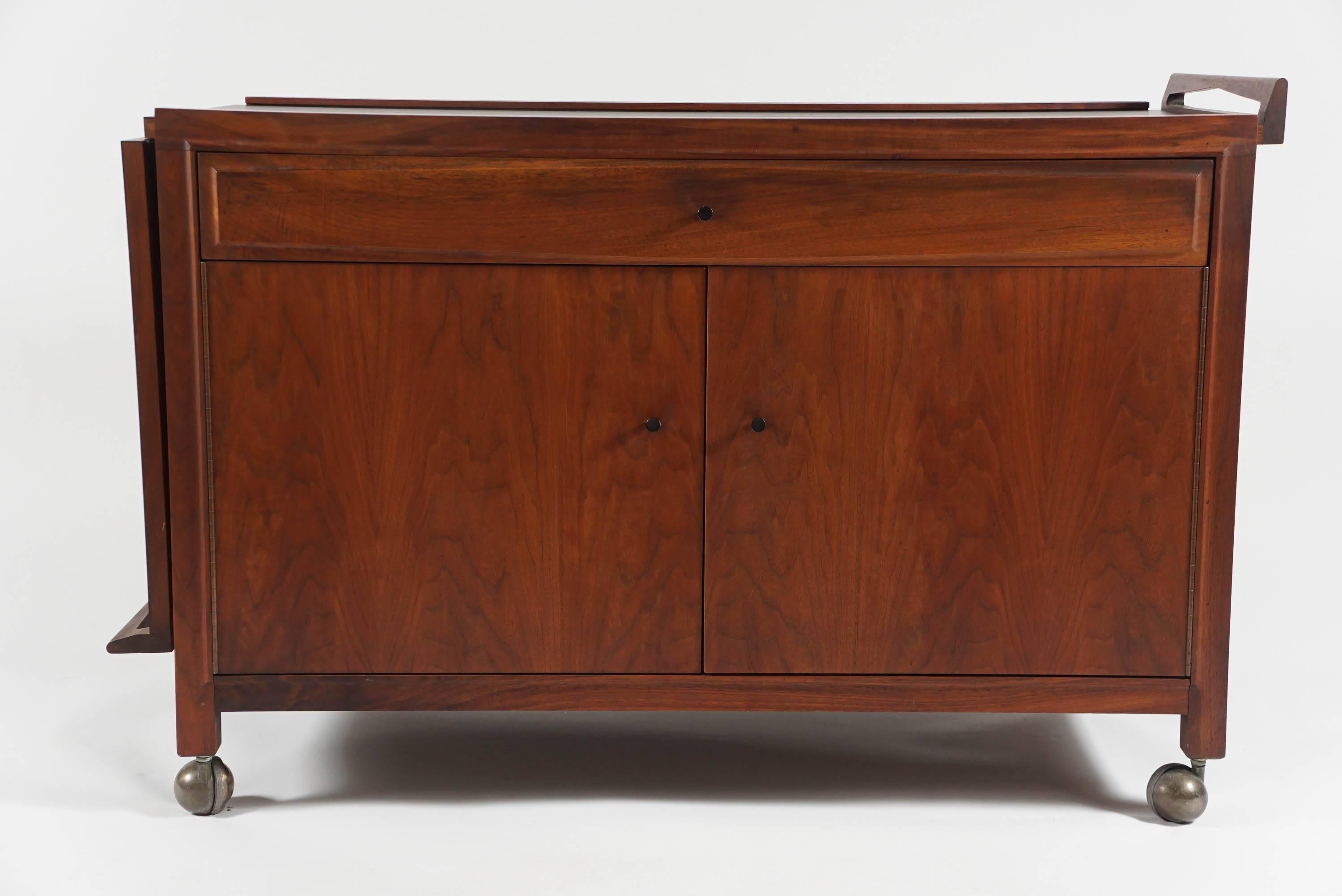 Mid-Century bar/Credenza with expandable top in walnut and black laminate.
Very clean lines and sculptural finger hold detail at both ends of the top. It has caster feet for easy moving. The top expands from 41