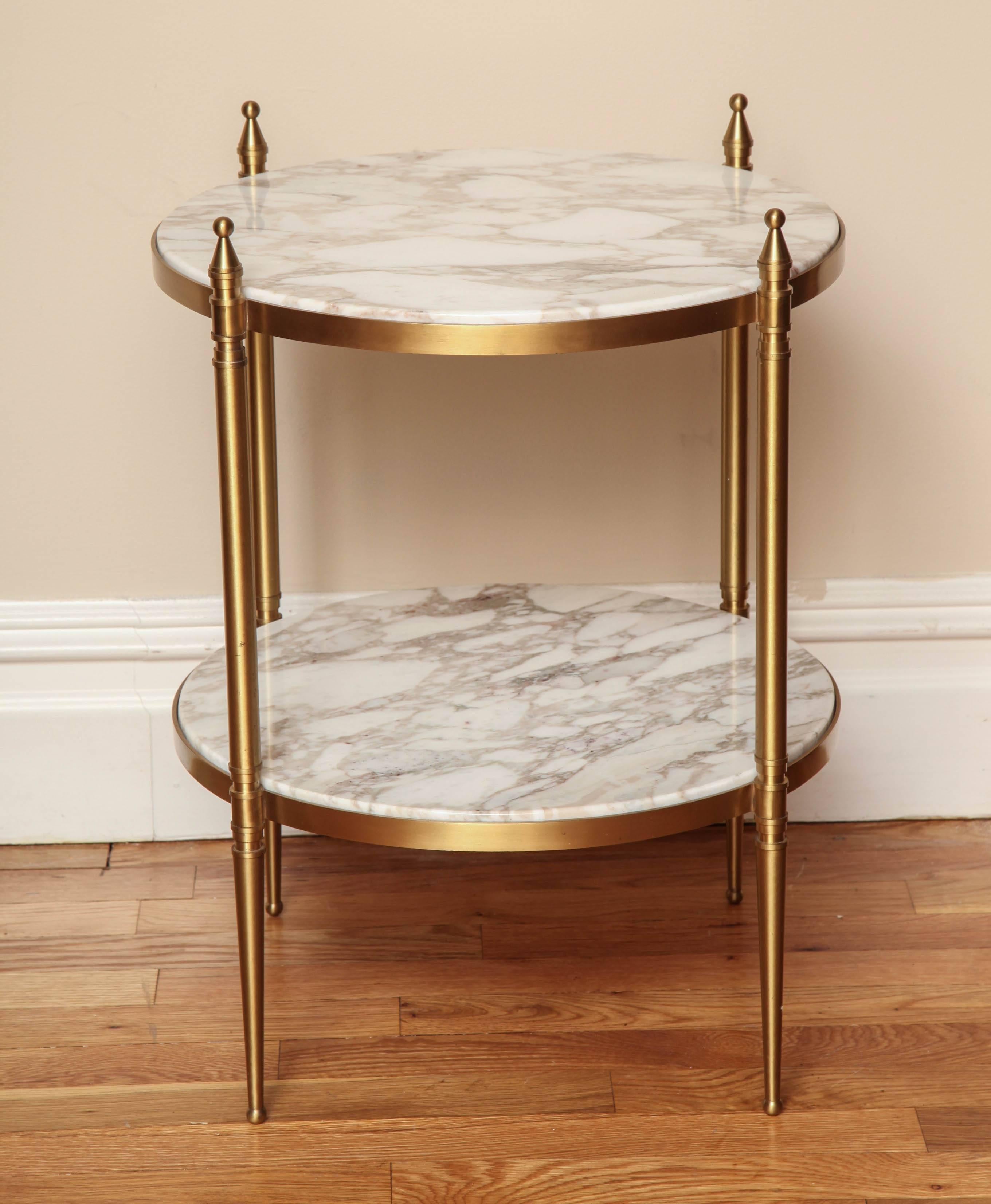 A round 2-tiered side table with marble surfaces inset in bronze frame and gold finials. The 2 surfaces are joined and supported by 4 round  legs tapering to ball point and ball shaped finials. Circa 1970.