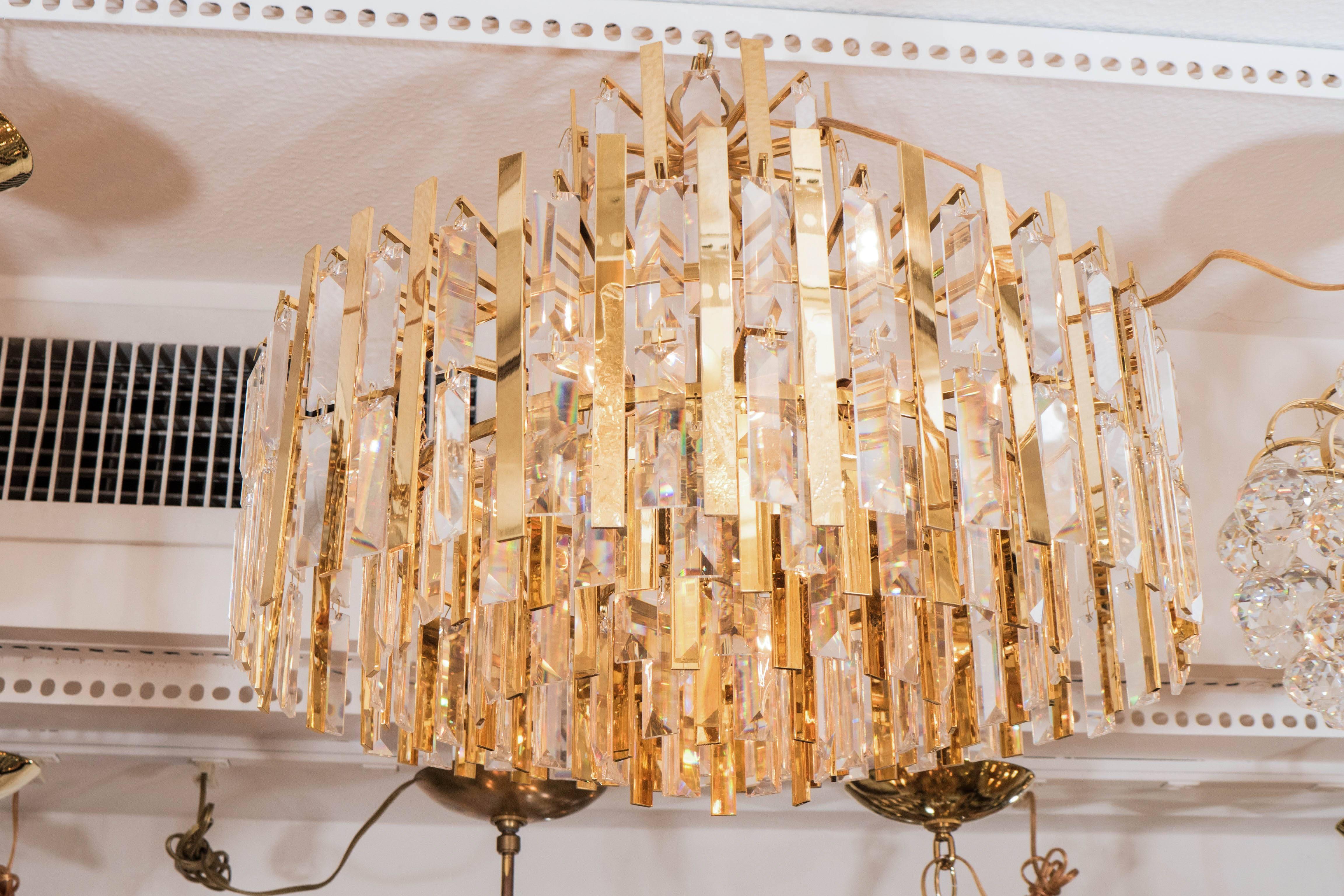 Brass chandelier composed of multiple suspended brass strips and crystal prisms.