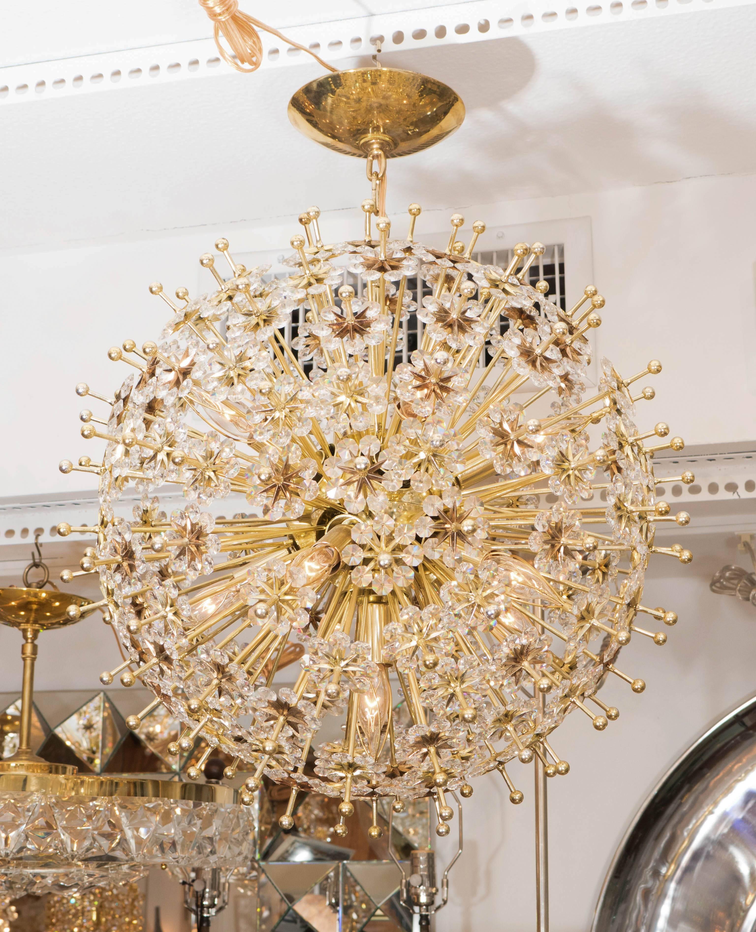 Brass starburst pendant ceiling fixture with rays terminating in flowers composed of cut crystal elements.