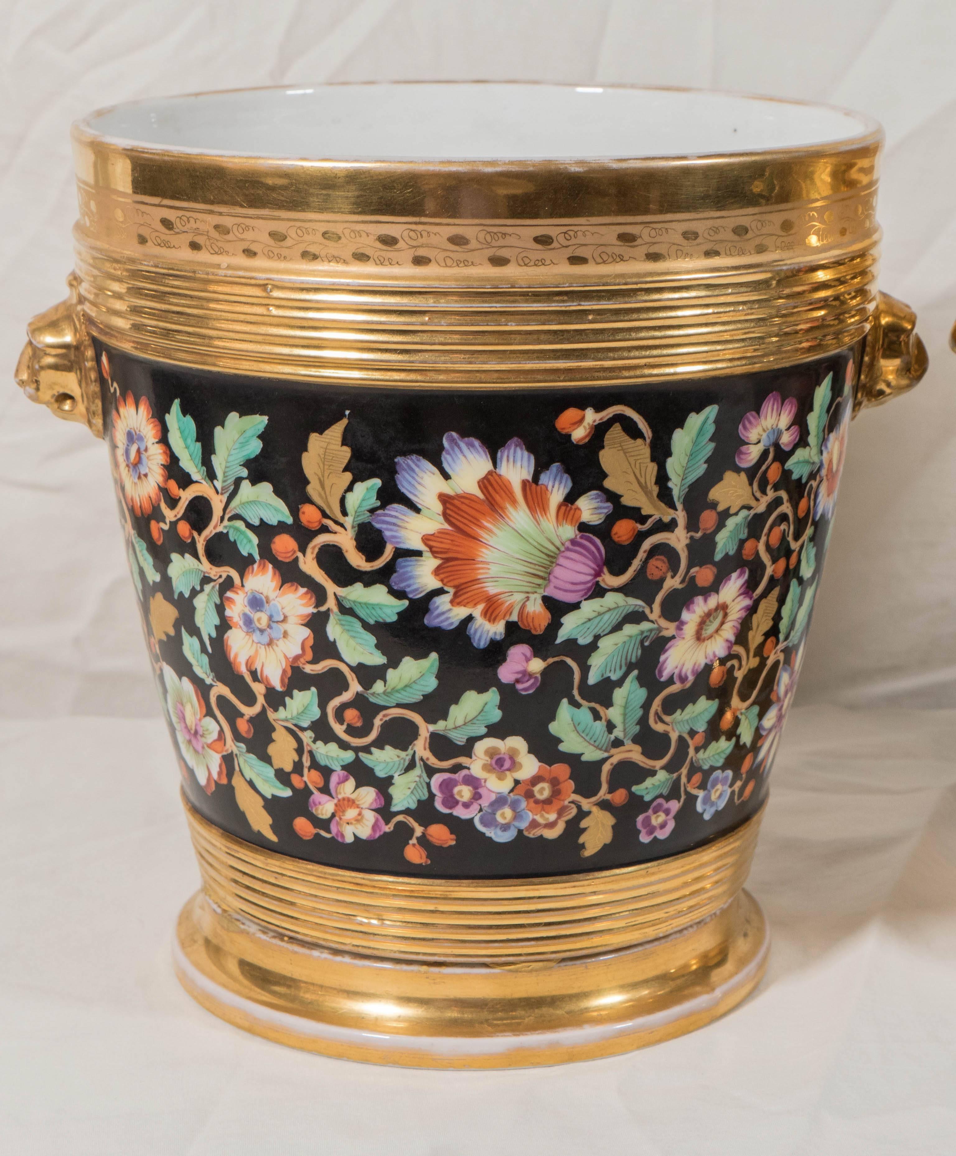 An important pair of early 19th century cache pots painted with vibrant colors showing a longtailed bird in a profusion of flowers on a black ground. The design is complemented by extensive gildng around the top, the base, and the lion's head