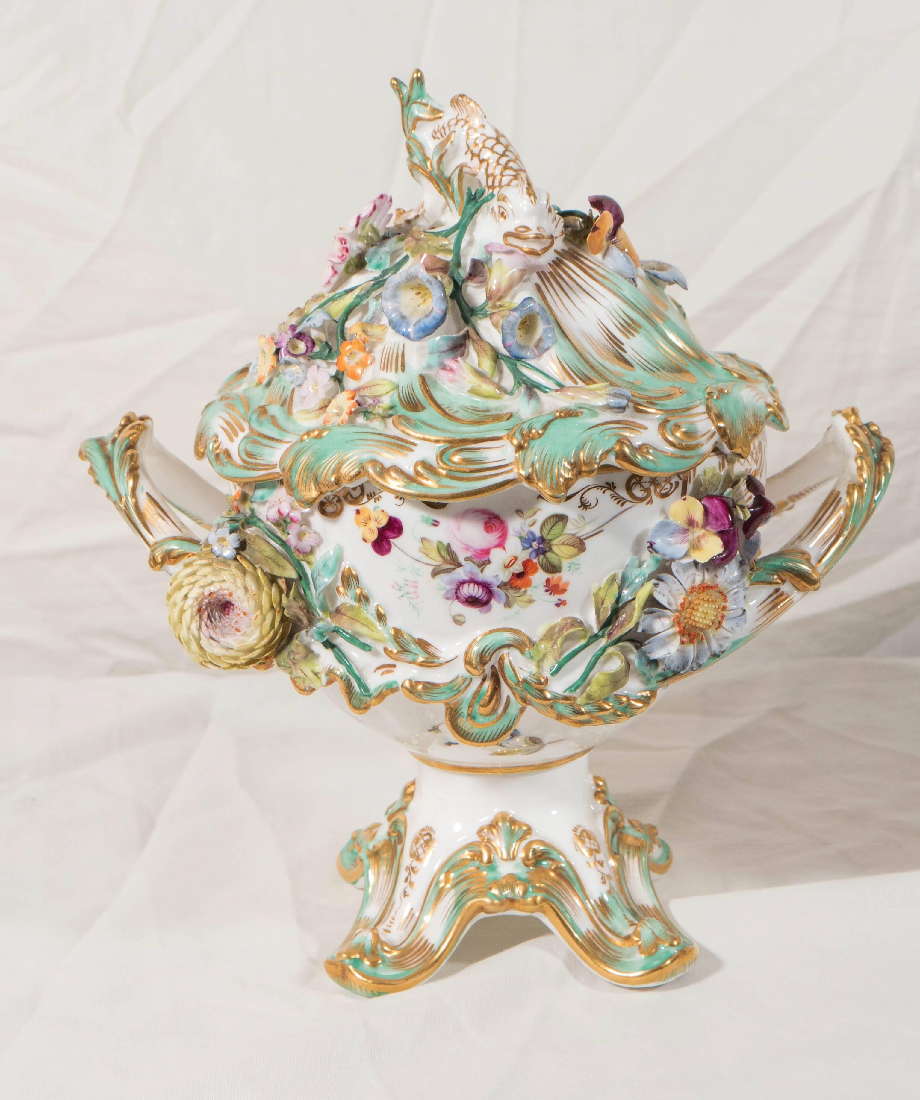 A pair of English porcelain flower-encrusted vases decorated in the Rococo style. The flowers on these vases were made separately and then applied to the surface of each piece. The handles are made to look like branches. The covers have dolphin