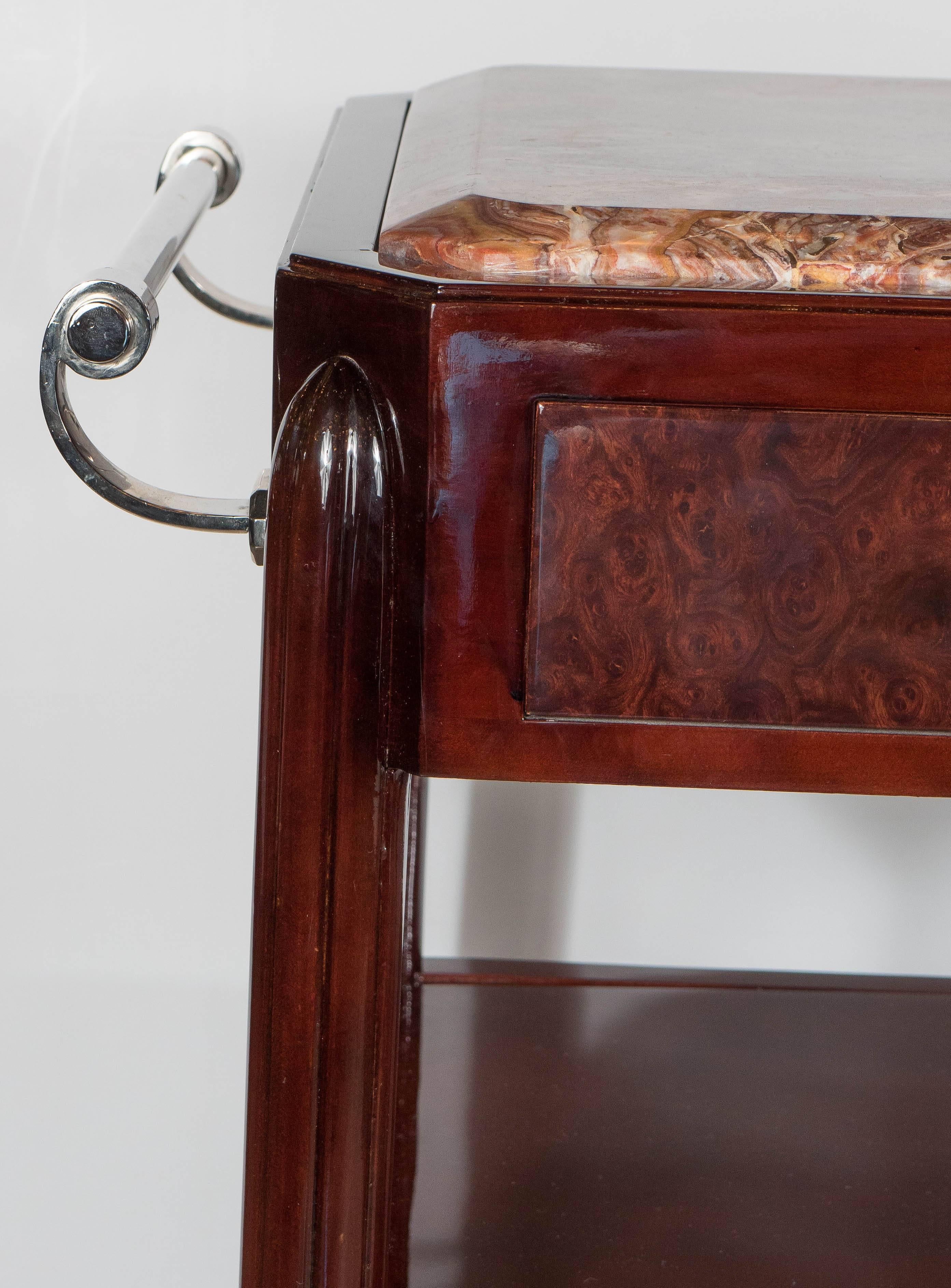An exquisite Art Deco bar cart in  book-matched mahogany and a gorgeous inset rounded exotic onyx top. Nickel fittings adorn the drawers and side handrail. The drawer facades are of burled amboyna wood on both sides. Three levels give this piece
