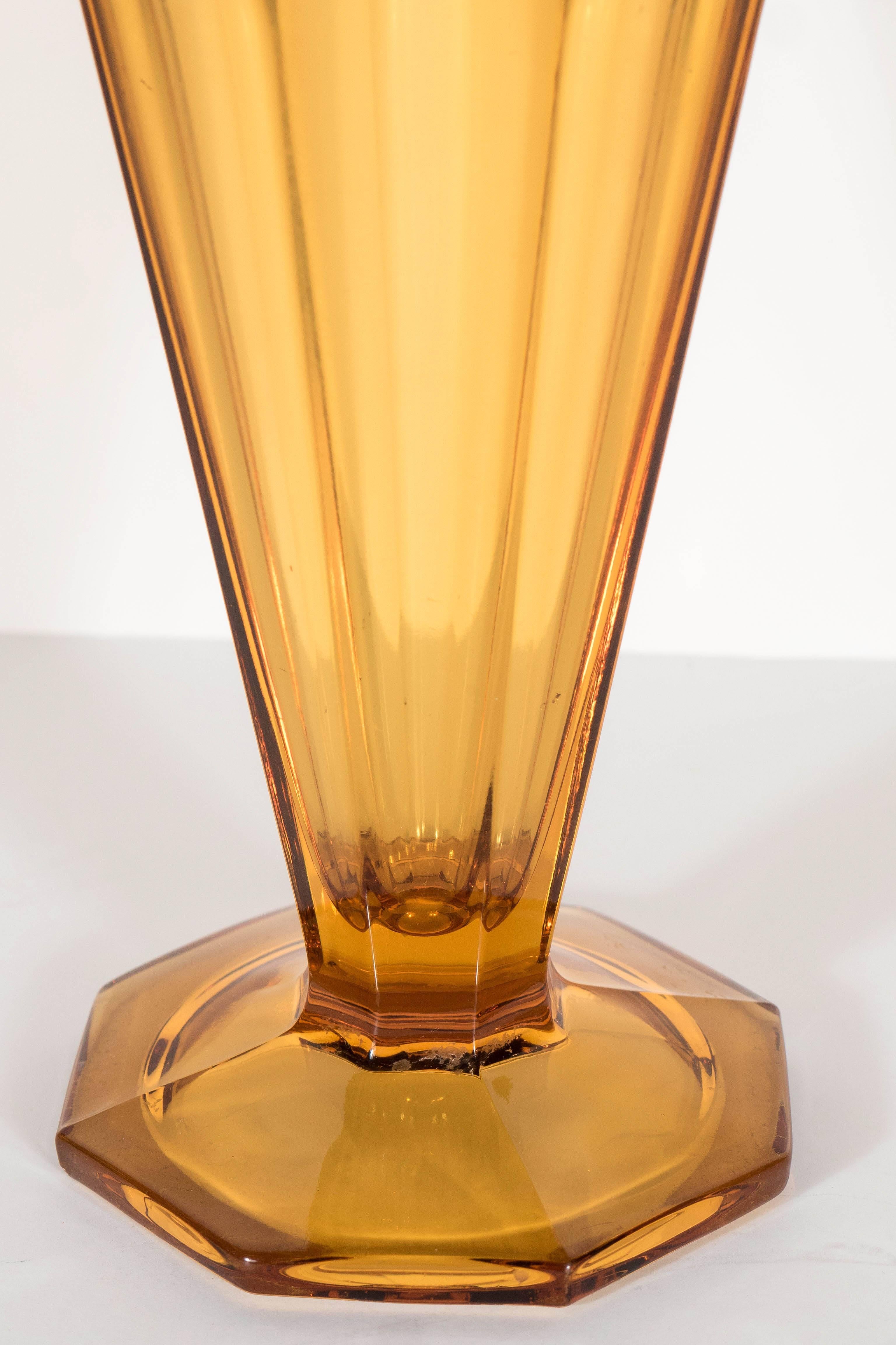 This vase features an octagon base with eight side panels forming the skyscraper style body of this vase. It is also accented with four extended ribbed details alternating on each panel. This vase is in perfect condition.