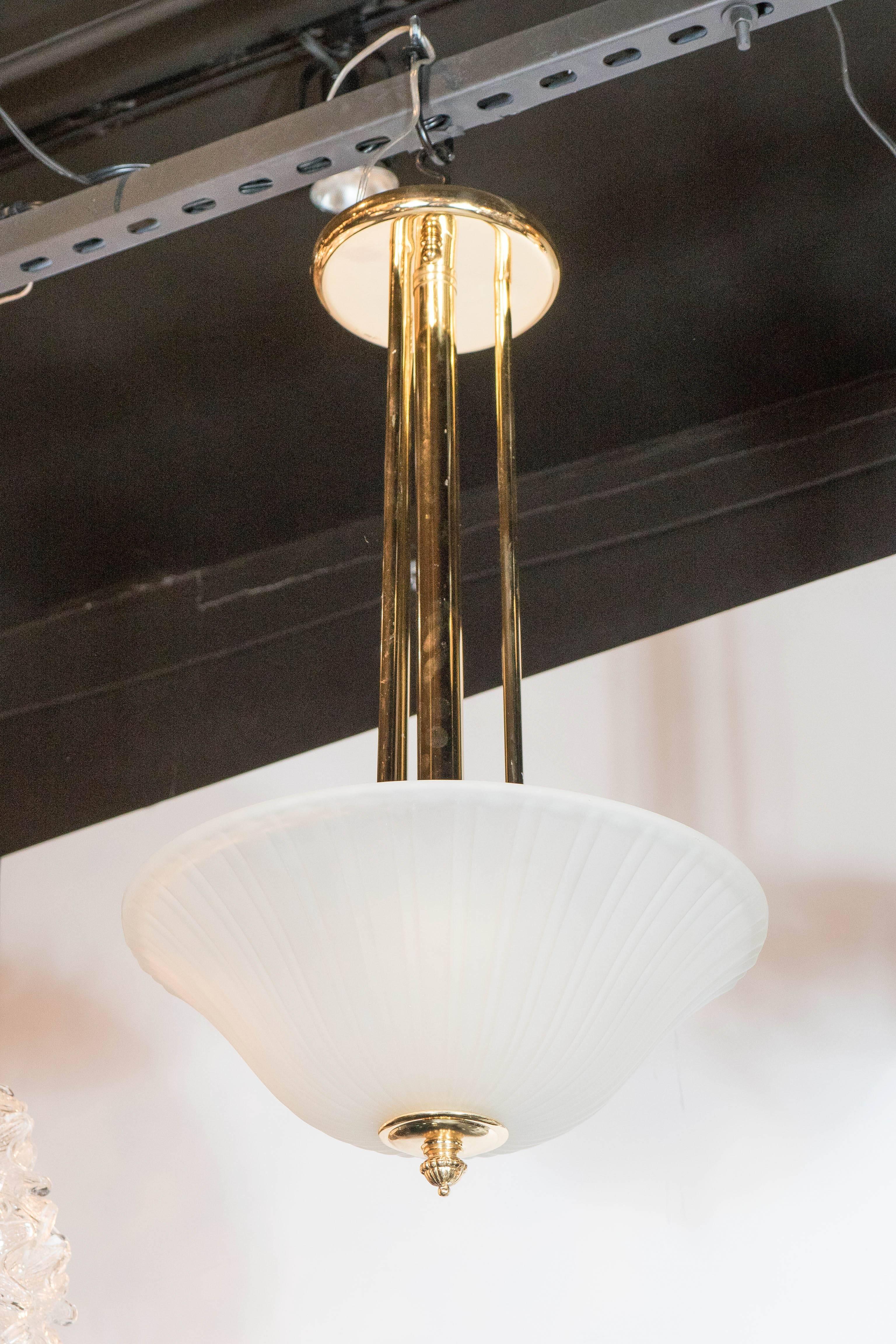 This elegant Art Deco pendant consists of a ribbed and fluted frosted glass dome supported by a detailed brass support, which connects to one wide and three supporting polished brass rods which connects to a flush mount cap. The clean lines on this