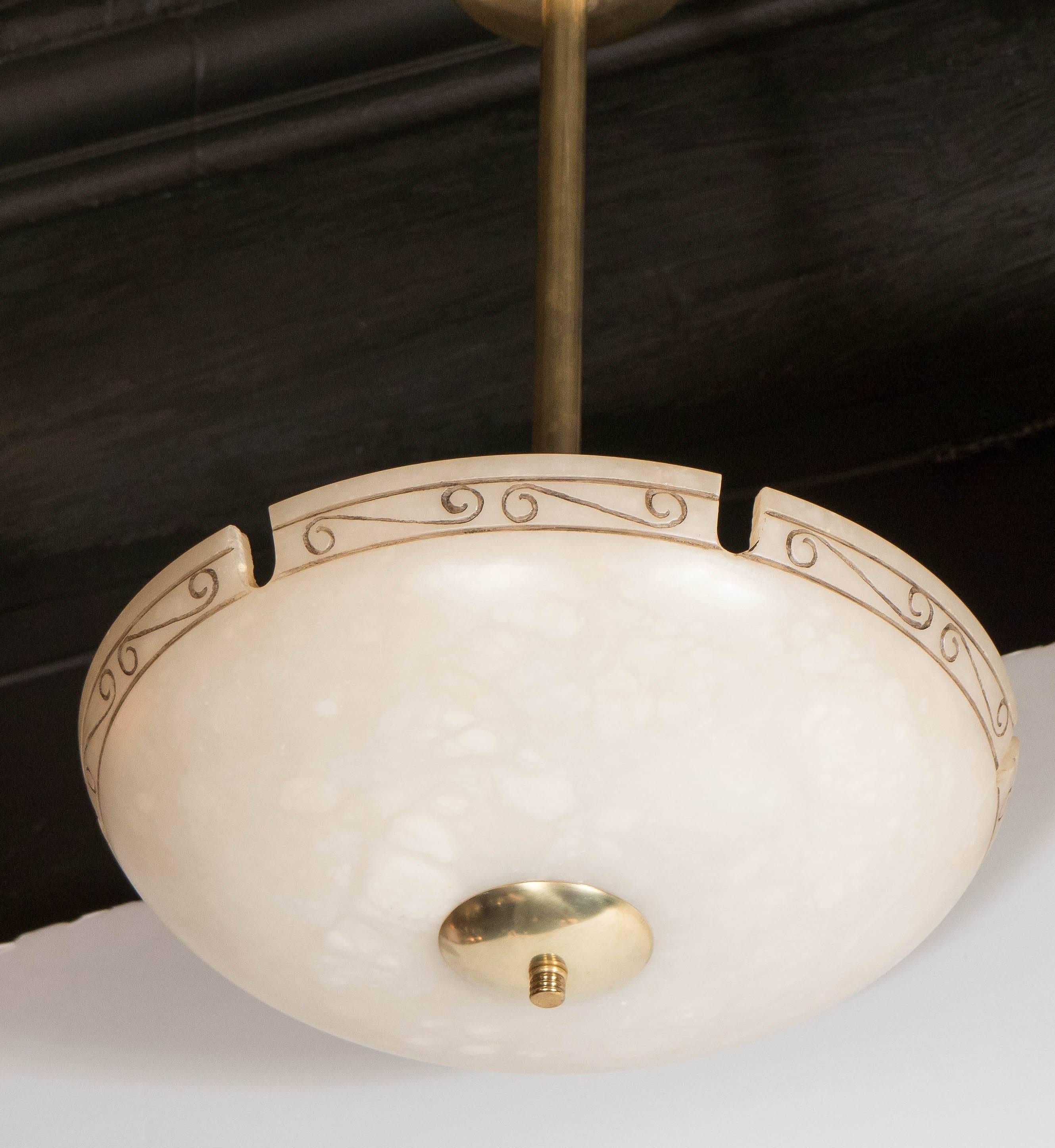 This exquisite Mid-Century Modernist chandelier features an alabaster dome shade with notch detailing and neoclassical scroll motif between each notch. It has antiqued brass fittings and is suspended from a rod which can be adjusted to suit the