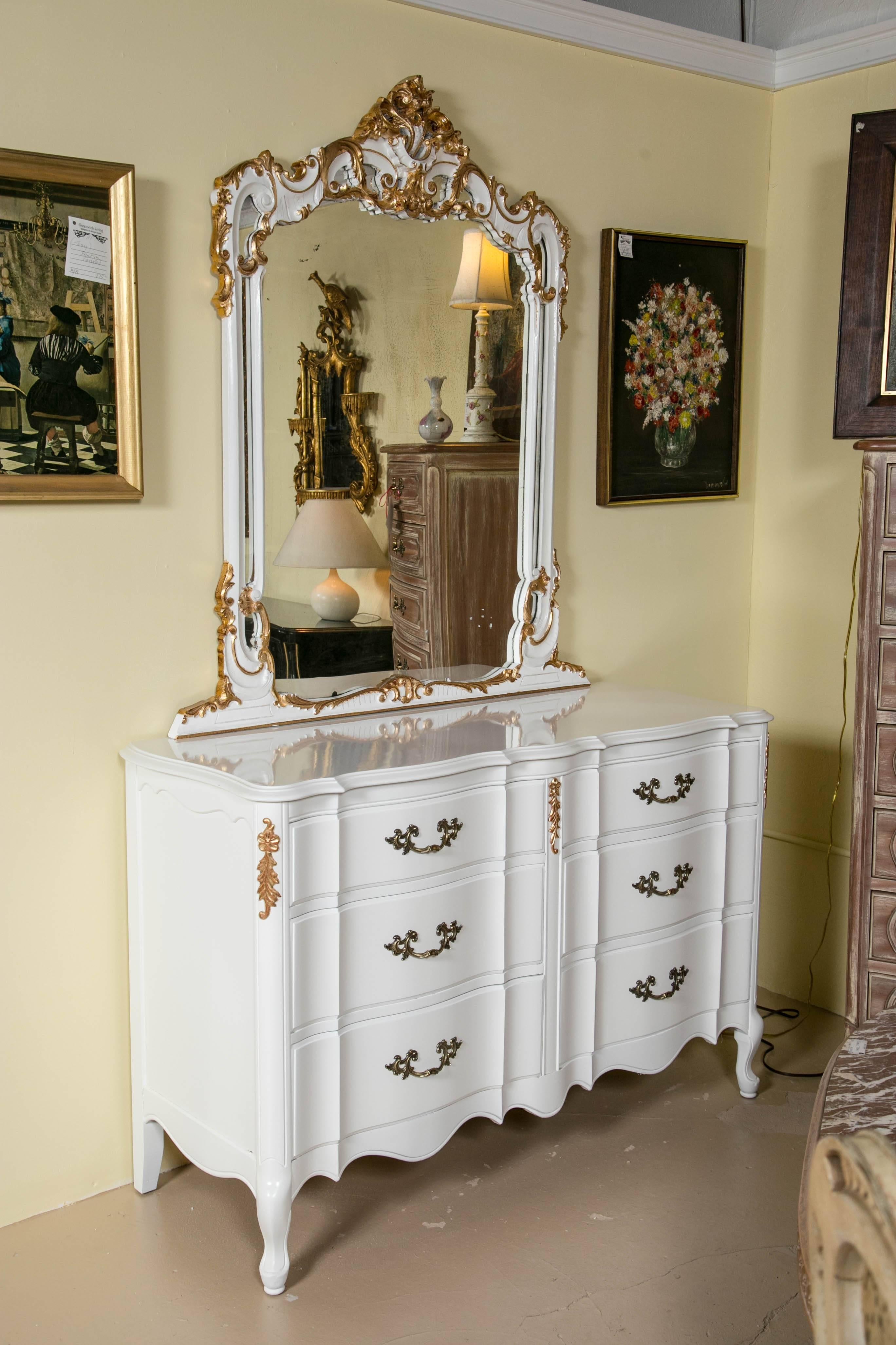 A white and gilt paint decorated double commode. Custom quality with solid wood case finely painted in a winter white with gilt gold hi lights and solid bronze pulls. The Louis XV style double commode has three by three drawers and a matching mirror