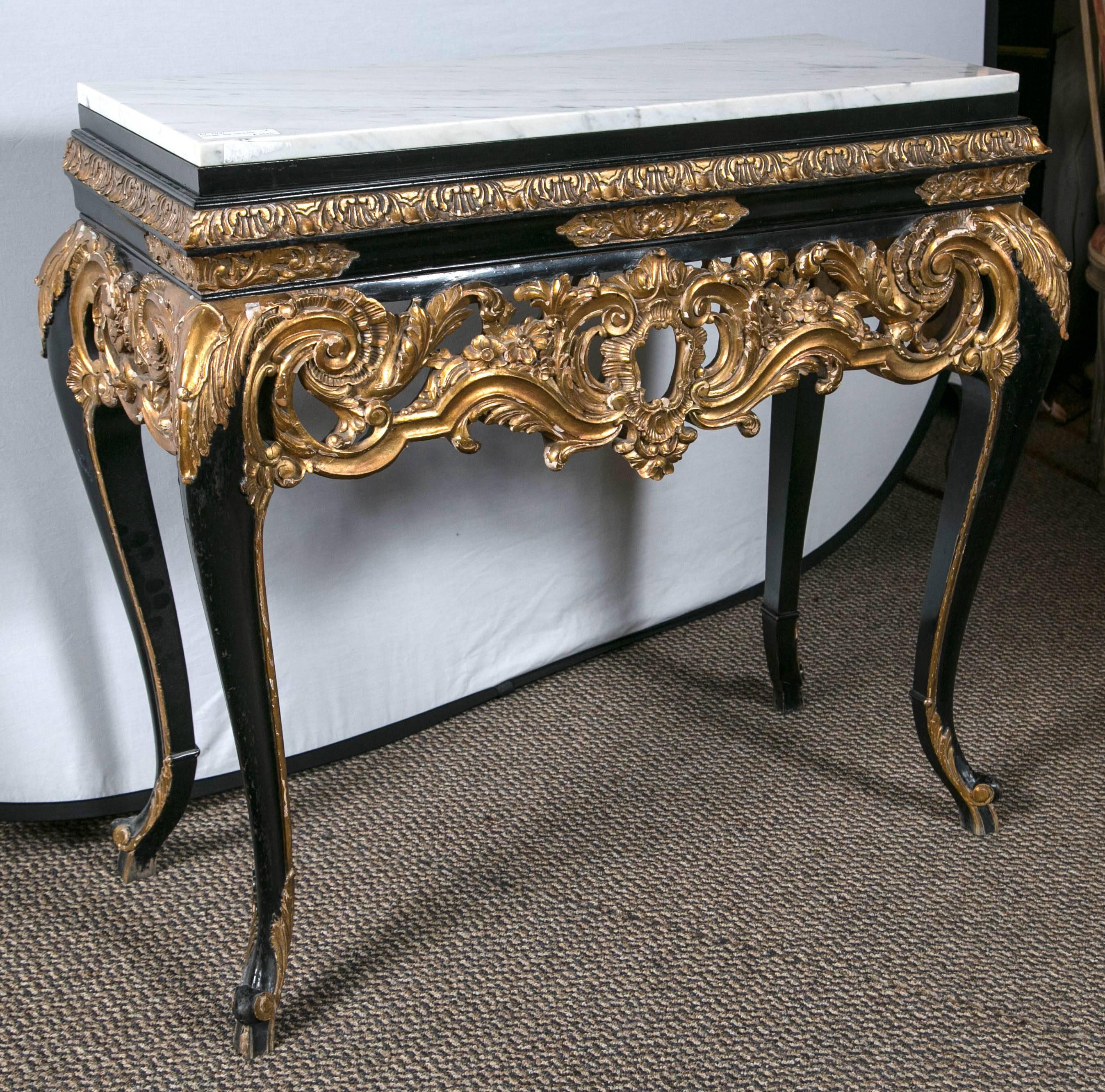 A fine gilt and ebony decorated marble-top console. This console has an elaborately carved skirt. A great and rare size. The petite console has elaborate detail fit for a grand room. The exquisiteness of the broad top leg that begins in a Louis XV