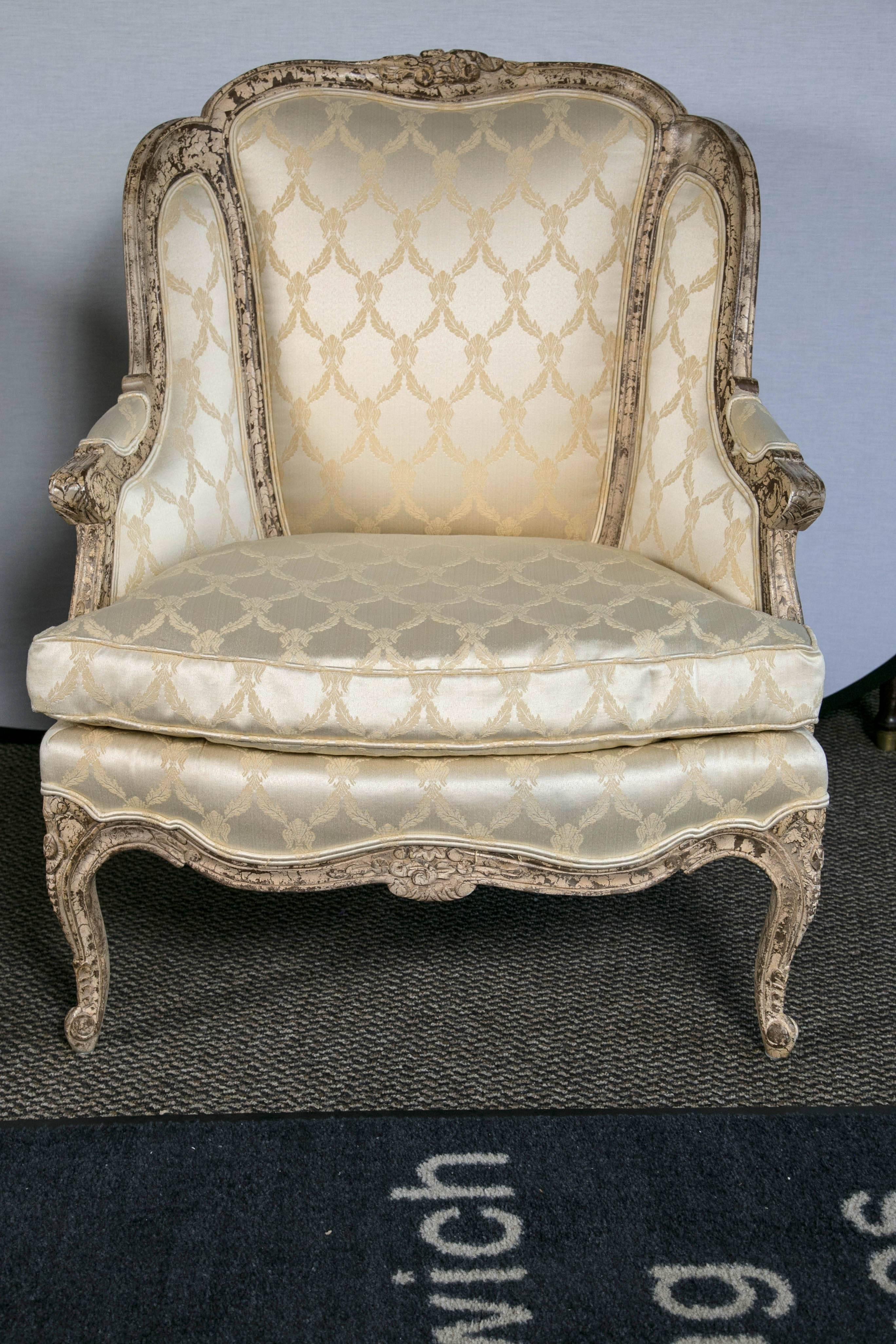 A pair of Louis XV style bergere chairs. Great silk fabric with wonderful leaf and flower design. Distressed paint decorated finish adding to the old world charm. The entire frame with fine distressed paint decorated design having detailed carvings