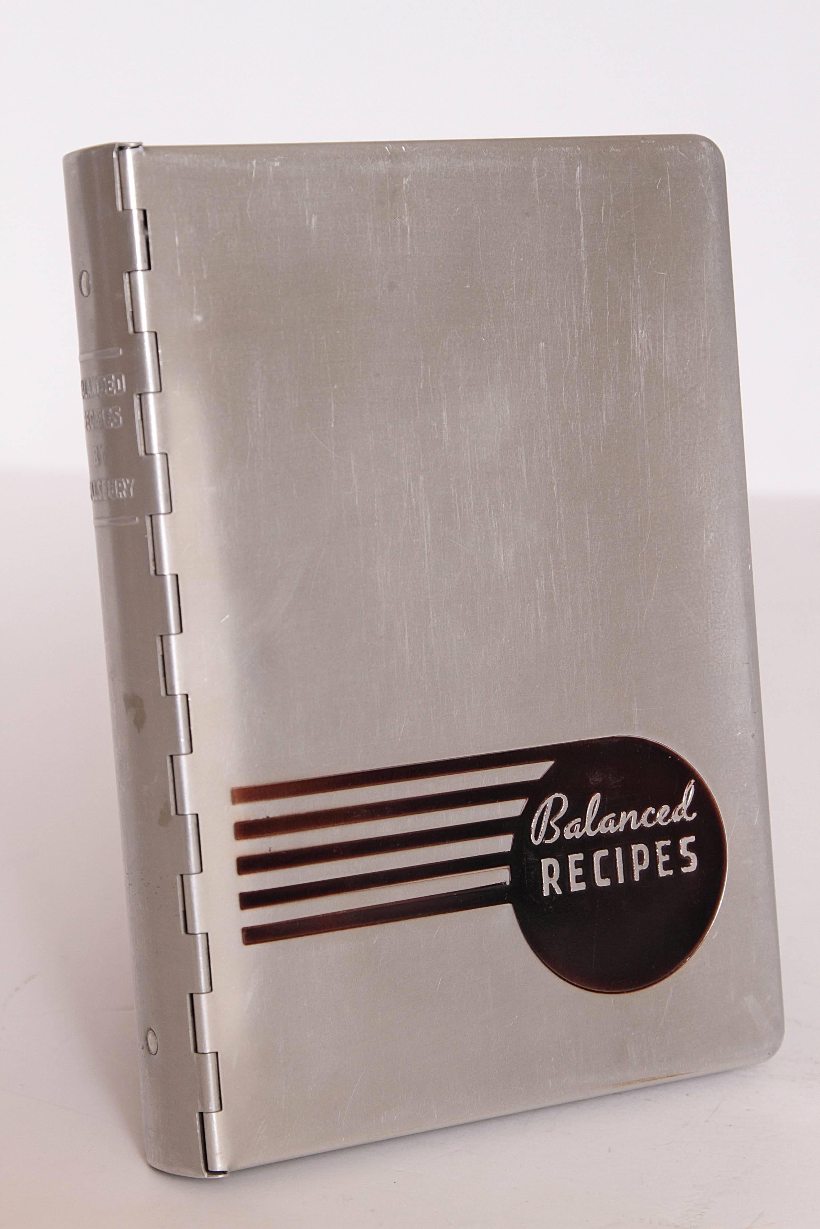Tabbed cookbook in a streamline hinged-aluminum case. The cookbook has an eleven-ring Binder with recipes in tabbed sections from desserts to main dishes, printed on overlapping slips of various sizes. Published in 1933, in conjunction with