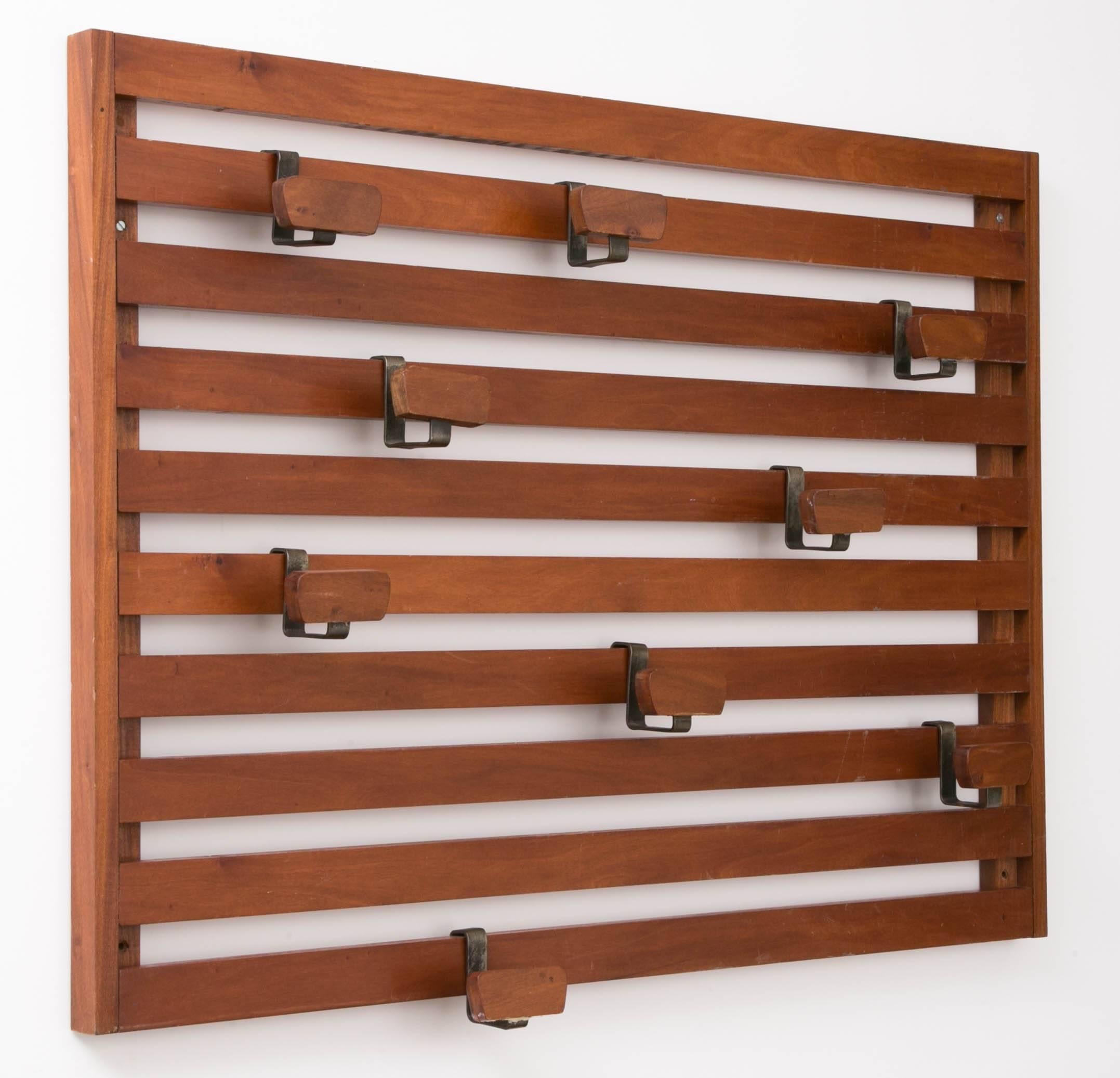 A mahogany and stainless steel mural coat rack with eight removable pegs.