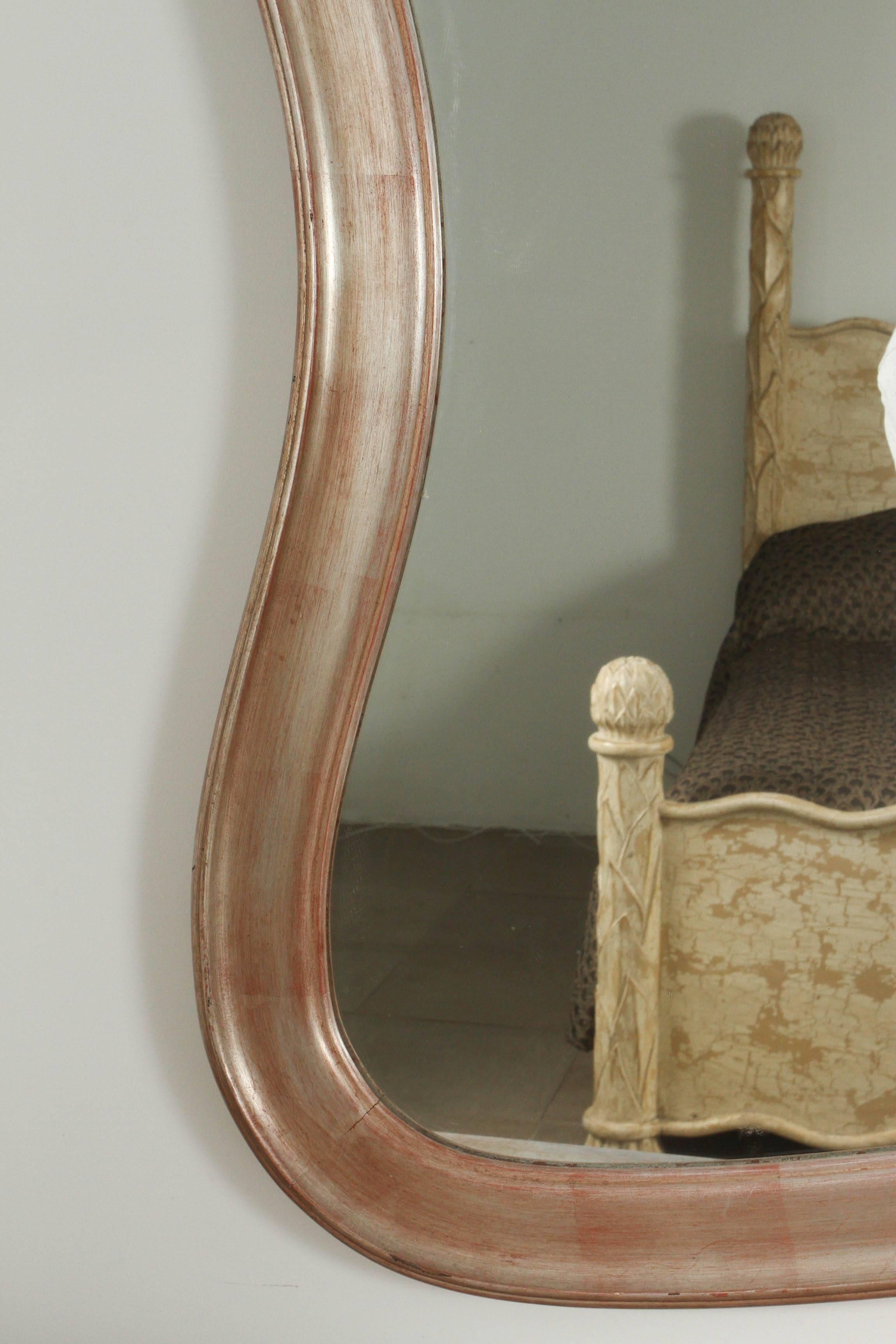 Rare Rococo modern mirror by James Mont.
This unusual mirror has an undulating frame retaining its original finish of silver leaf with a rosy overglaze.

 
