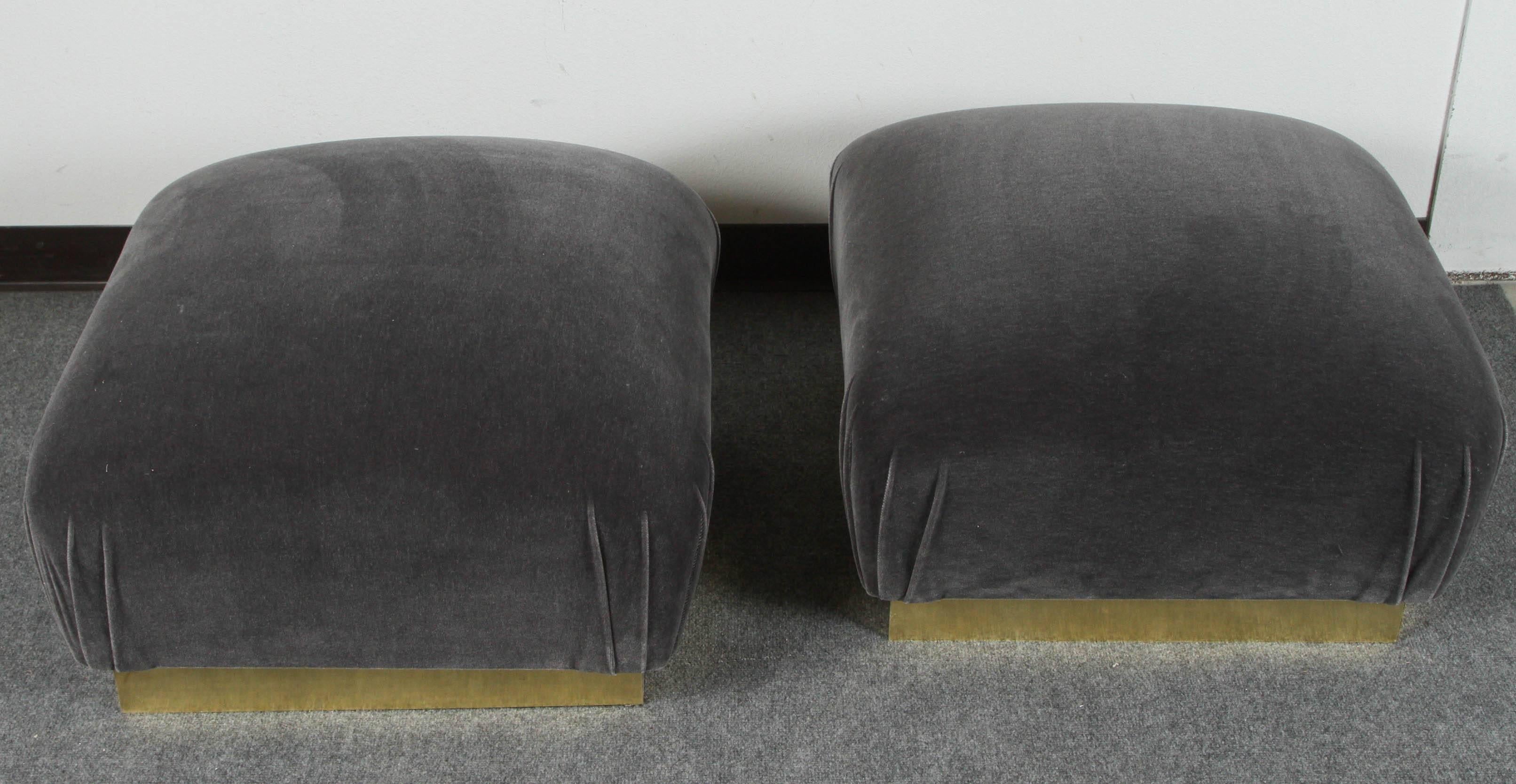 Pair of pouf ottomans by Steve Chase. They are upholstered in a grey mohair velvet and the brass trim gives them a tailored appearance.