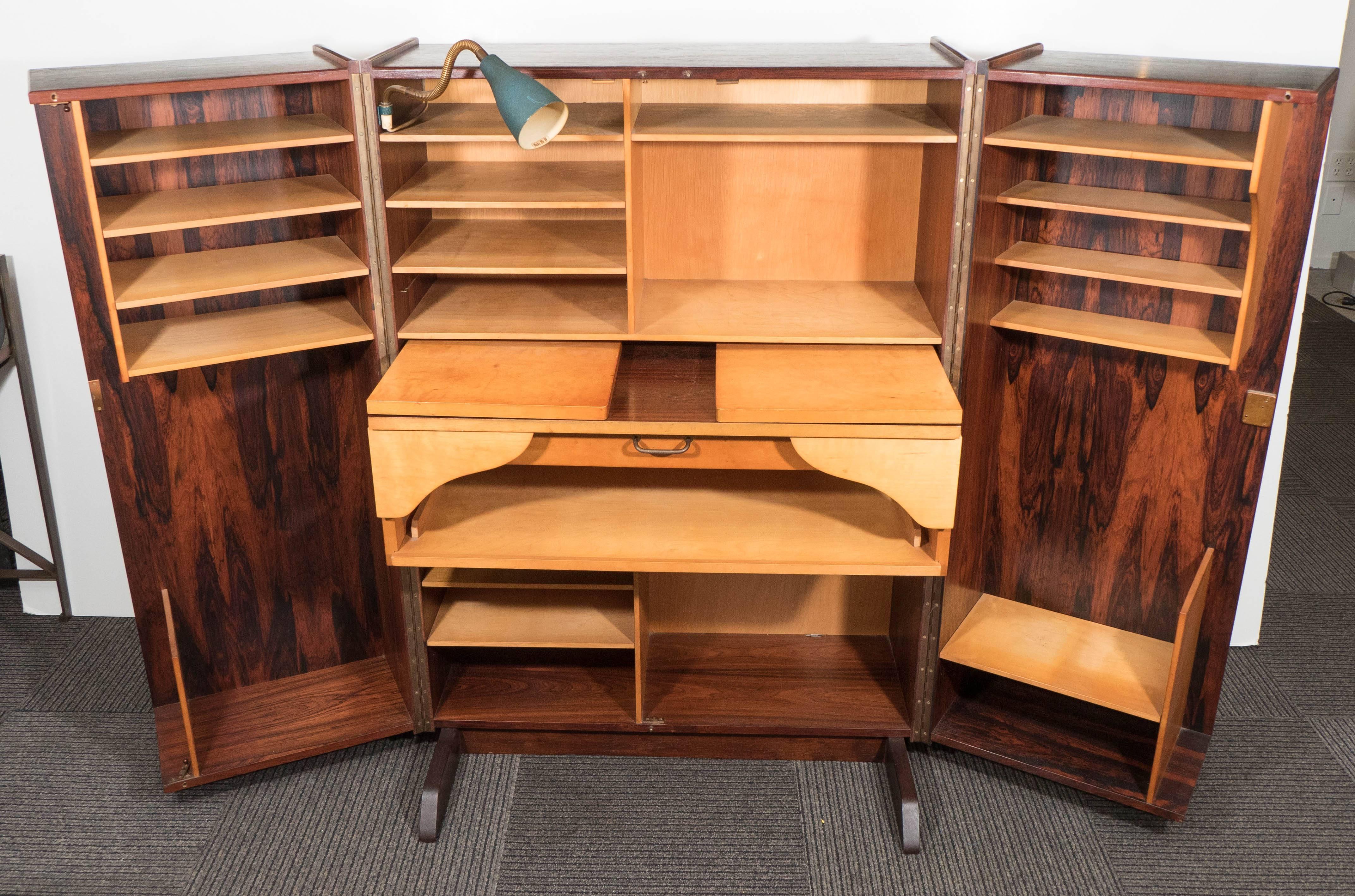 A vintage Norwegian hideaway desk, produced circa 1960s, in the Scandinavian Modern style; this versatile desk can compact into box, veneered in rosewood and expand into a full office with extensive shelving space, desk and foldable leaves, an