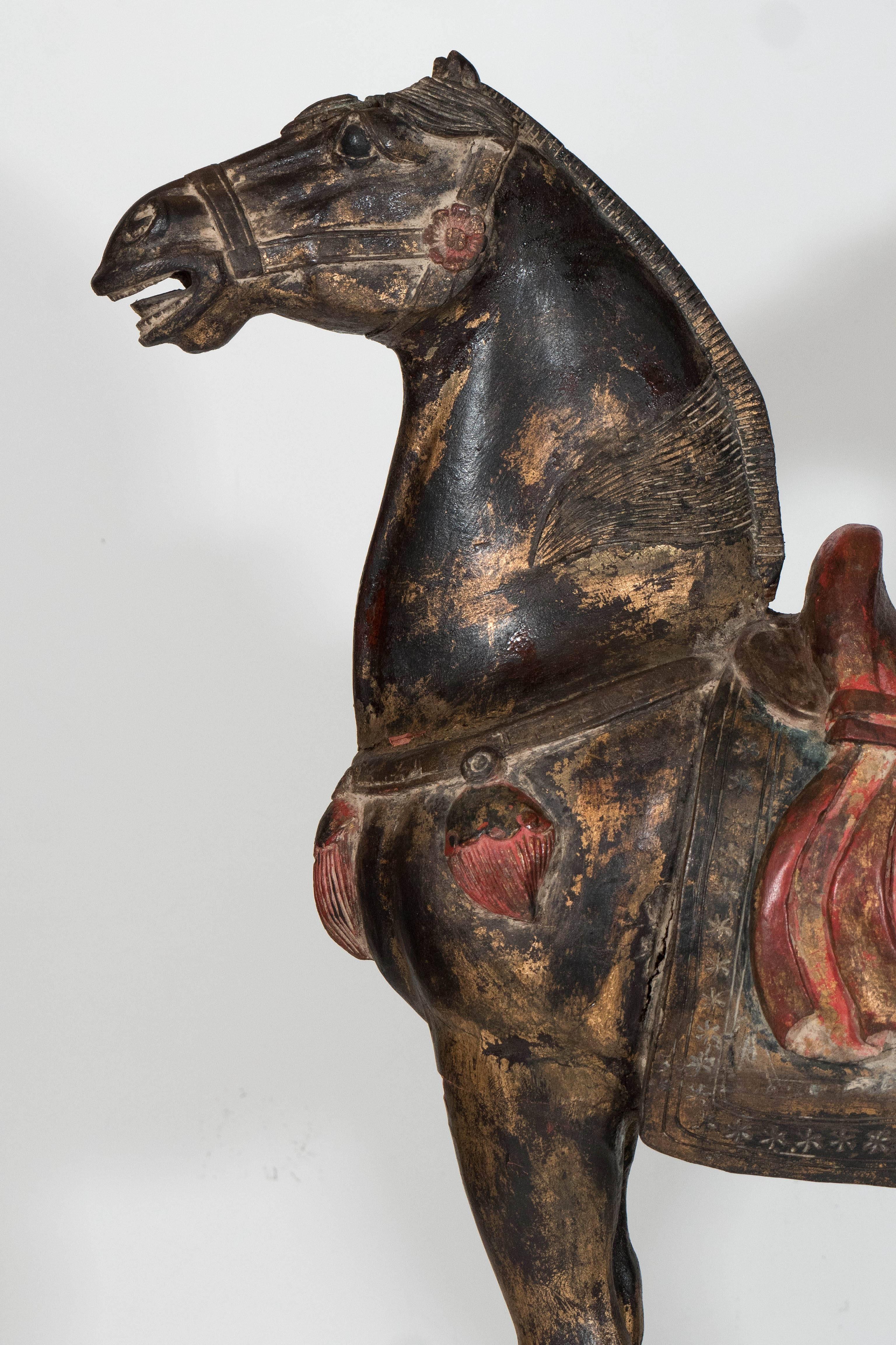 This sculptural, finely carved wooden horse, visually channeling the styles of the Tang Dynasty, was produced within the early 1900s in China, with applied gilding and polychrome. A wonderful piece in good condition, with a small amount of cracking