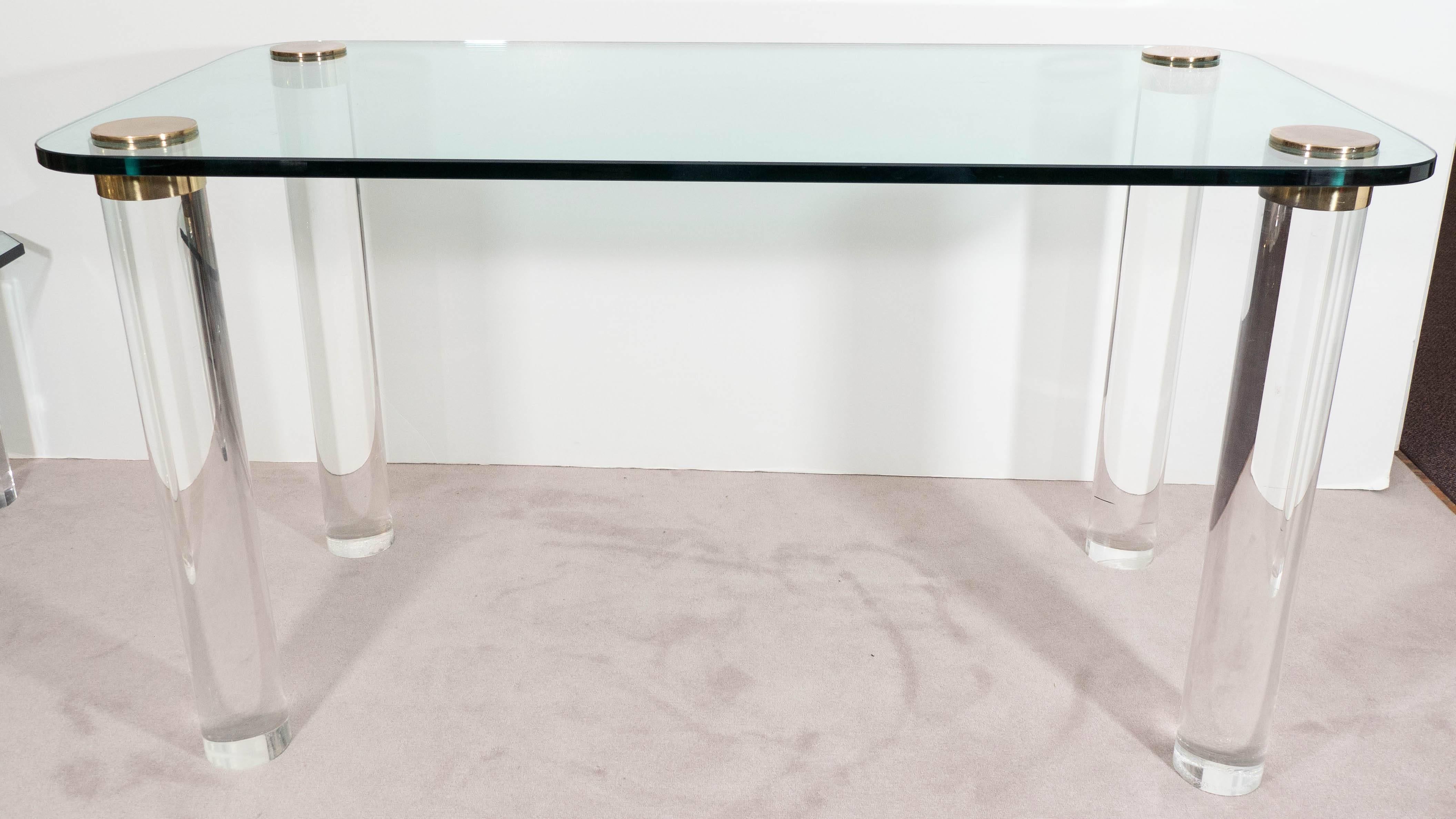 A vintage console table and desk, produced circa 1970s by Pace Collection, with round edge glass top, inset by cylindrical legs in Lucite, capped with brass discs. Good condition, any wear consistent with age and use, including some scratches to the