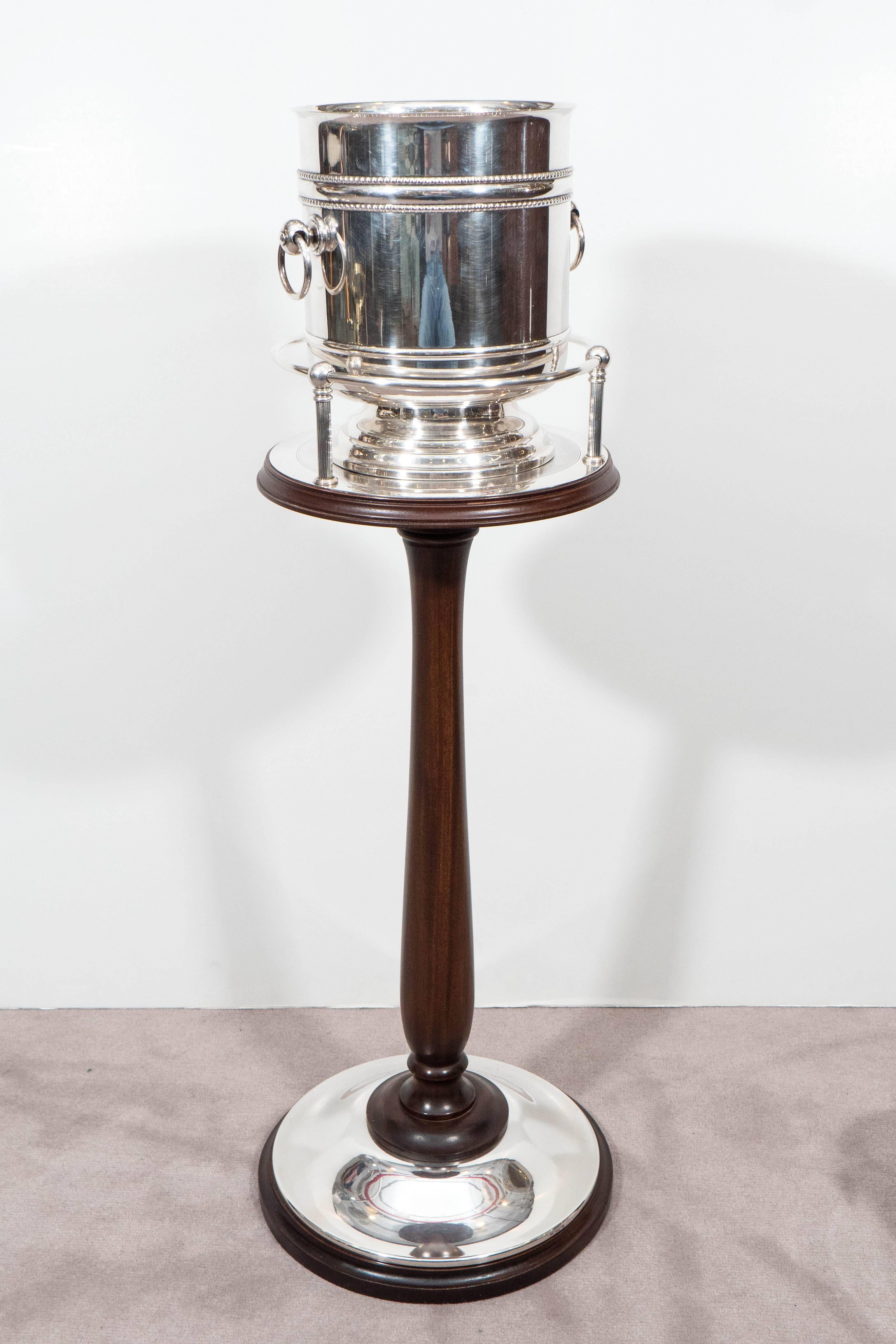 Very rare Art Deco champagne buckets in silver plate, each with ring handles on stepped pedestal bases, produced circa 1930s by Christofle, on mahogany stand, which features a silver plate top with circular gallery, over a turned, baluster form stem