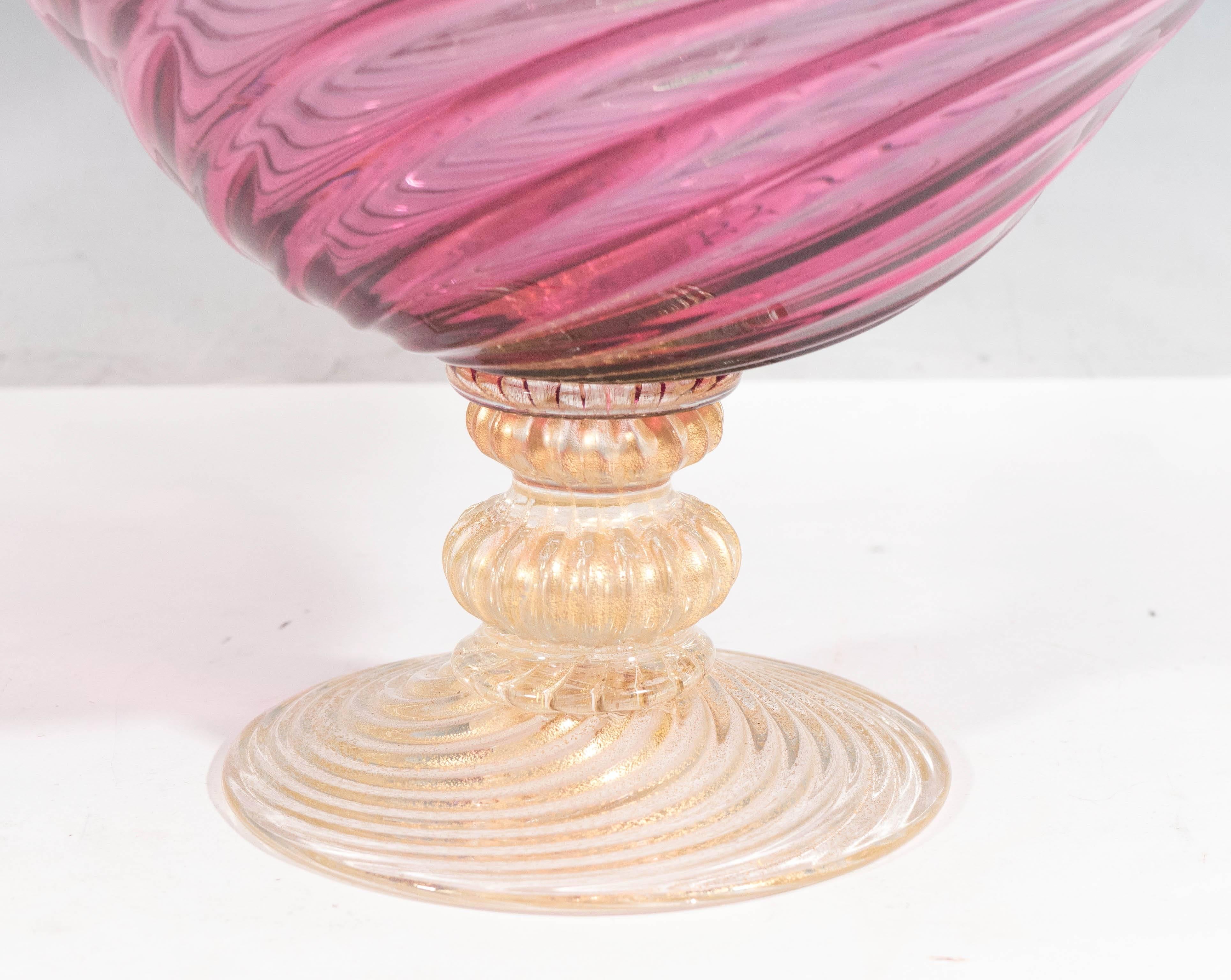 An Italian vintage glass bowl in pink, produced in Venice by Vetreria Fratelli Toso, circa 1960s, with frilled detail to the rim, over the fluted swirled body, raised on a pedestal base, infused with gold flakes. Marked with labels [Venetian