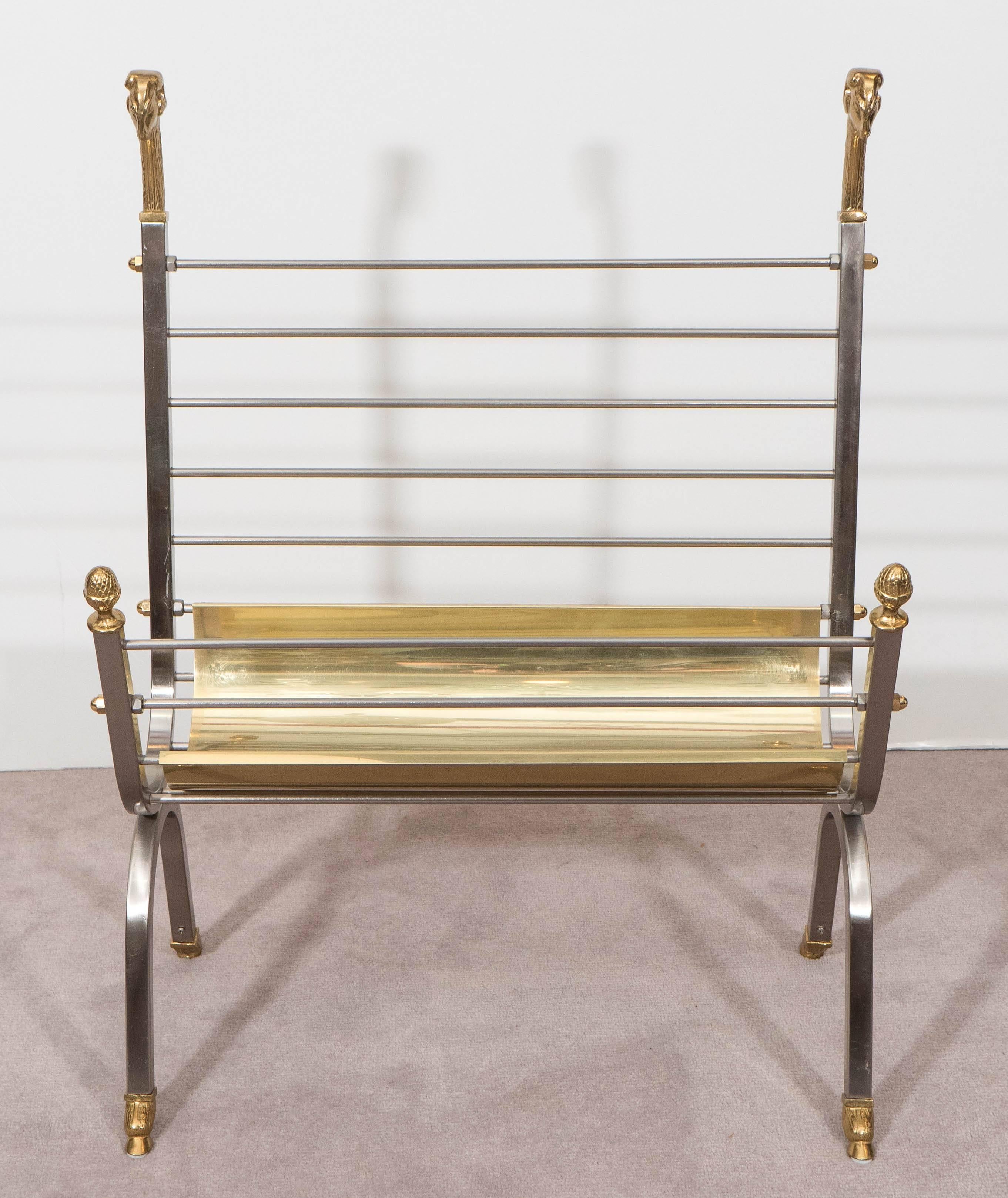A vintage magazine rack, produced in Italy circa 1970s, with details of ram's heads and acorn finials, surmounting the brushed steel frame and rack on hoof feet, inset by polished curved brass insert. Markings include label [Made in Italy] affixed