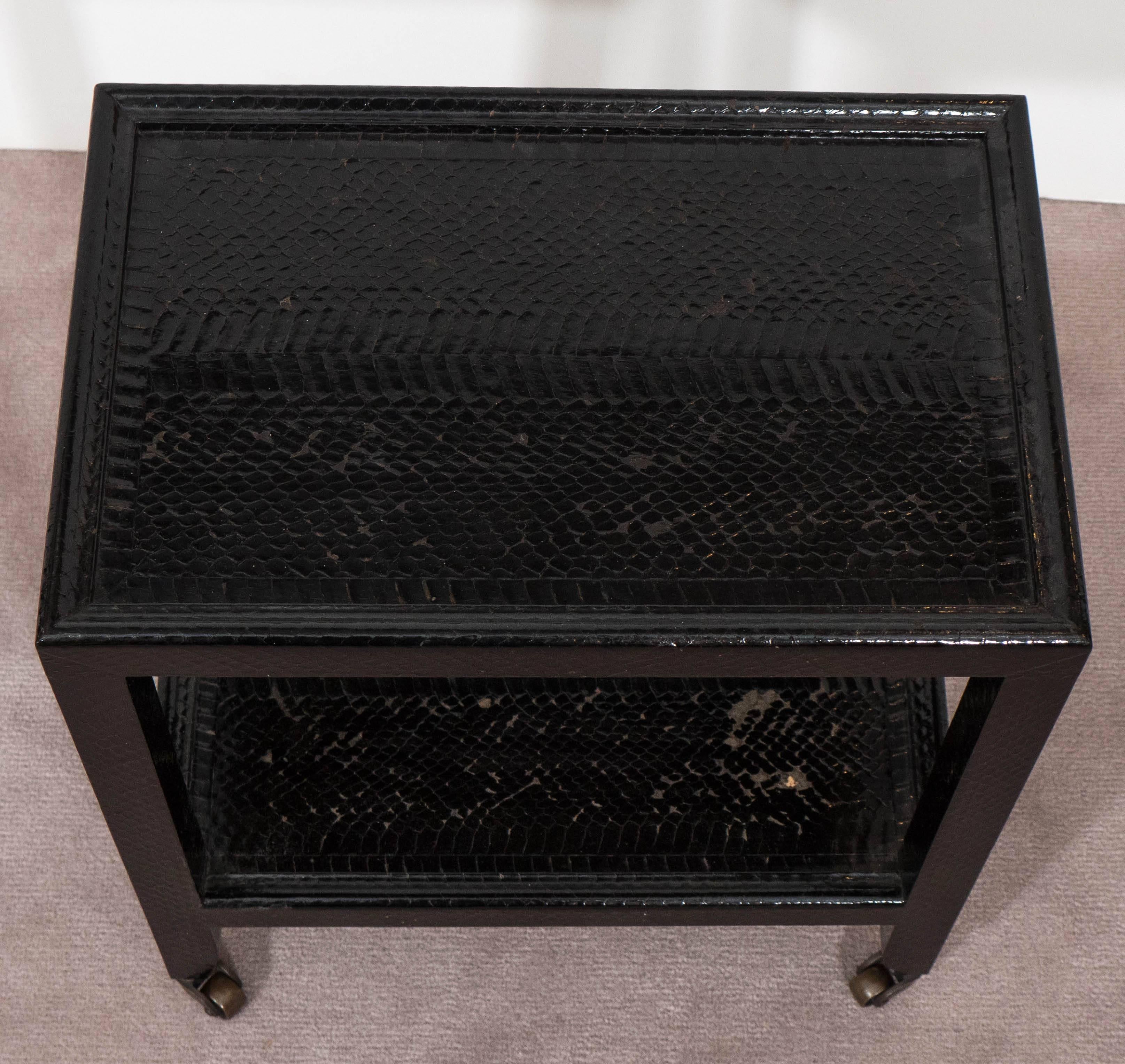 A small-scale two-tier telephone table, produced by Karl Springer circa 1980s, in black snakeskin on brass casters. Markings include signature and date [Karl Springer 1983], affixed to the underside of the bottom tier. Good condition, consistent