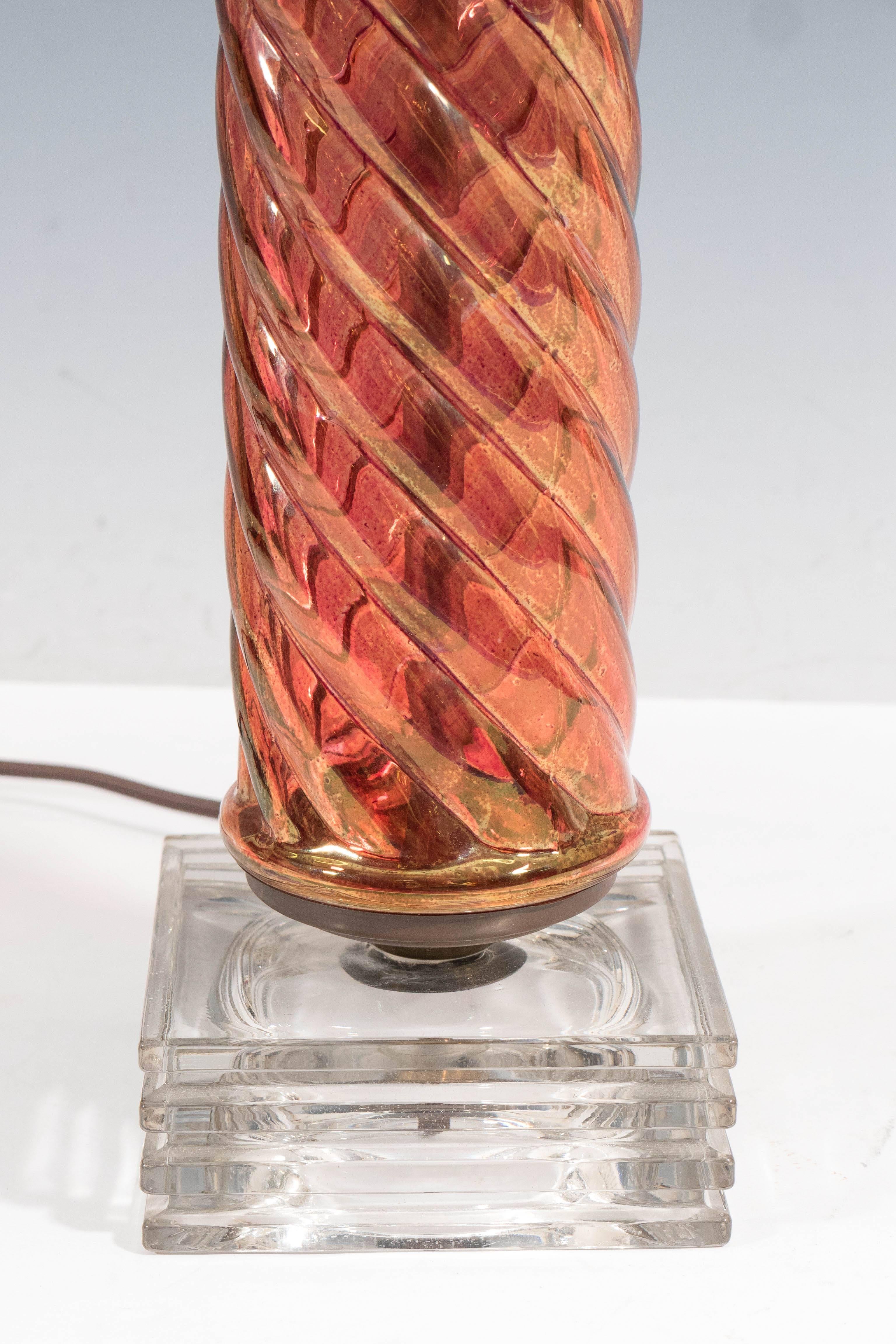A pair of table lamps, each in iridescent amber toned glass, in the form of serpentine columns, capped with brass, on stepped glass bases. Wiring and sockets to US standard, each requires one Edison base bulb. Good vintage condition, with visible