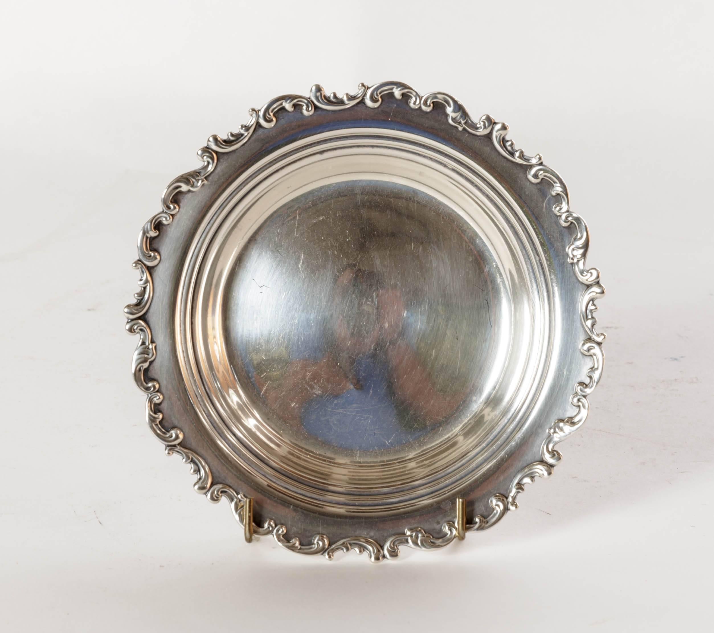 1920s sterling silver wine coaster with scalloped Baroque influenced rim. The inner rim has a plain double border, the sides taper to a slightly convex bottom. Very decorative and practical to protect a table cloth or table surface. The exterior