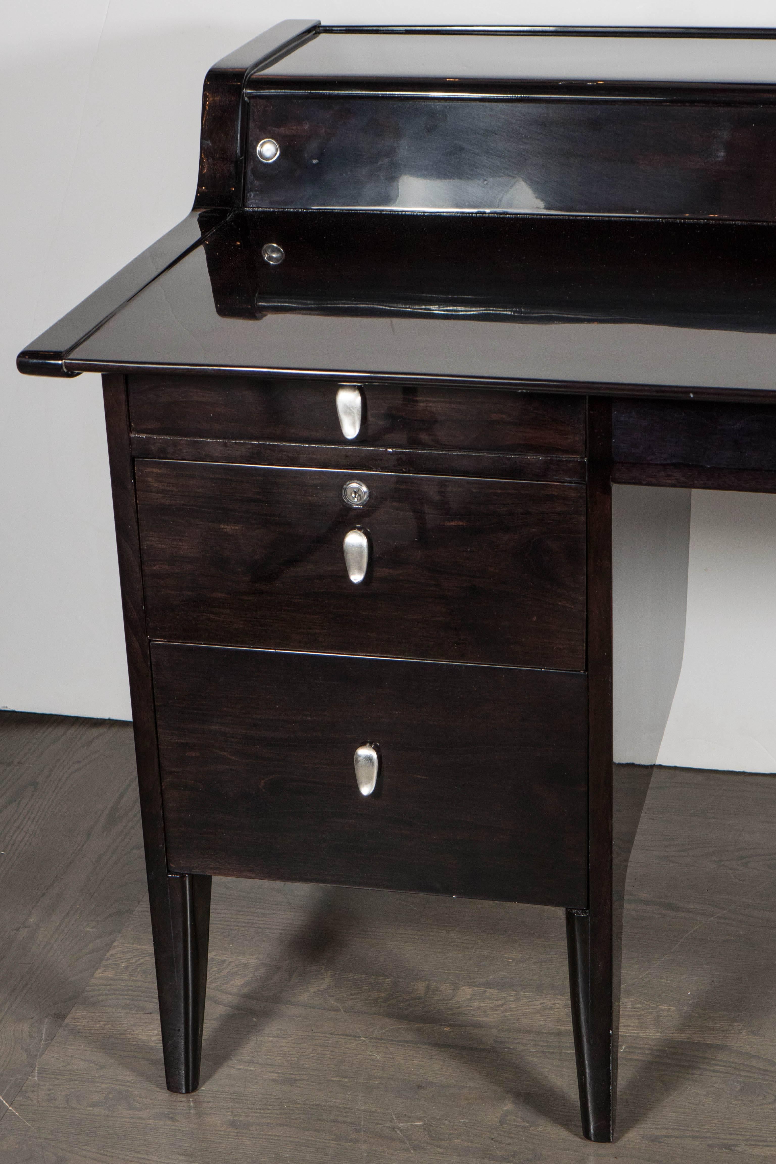 This Mid-Century Modern desk was designed by John Van Koert for the Drexel Company. The desk is ebonized birch with a generous writing surface and also features secretary compartments behind sliding panels. This piece also features original nickel