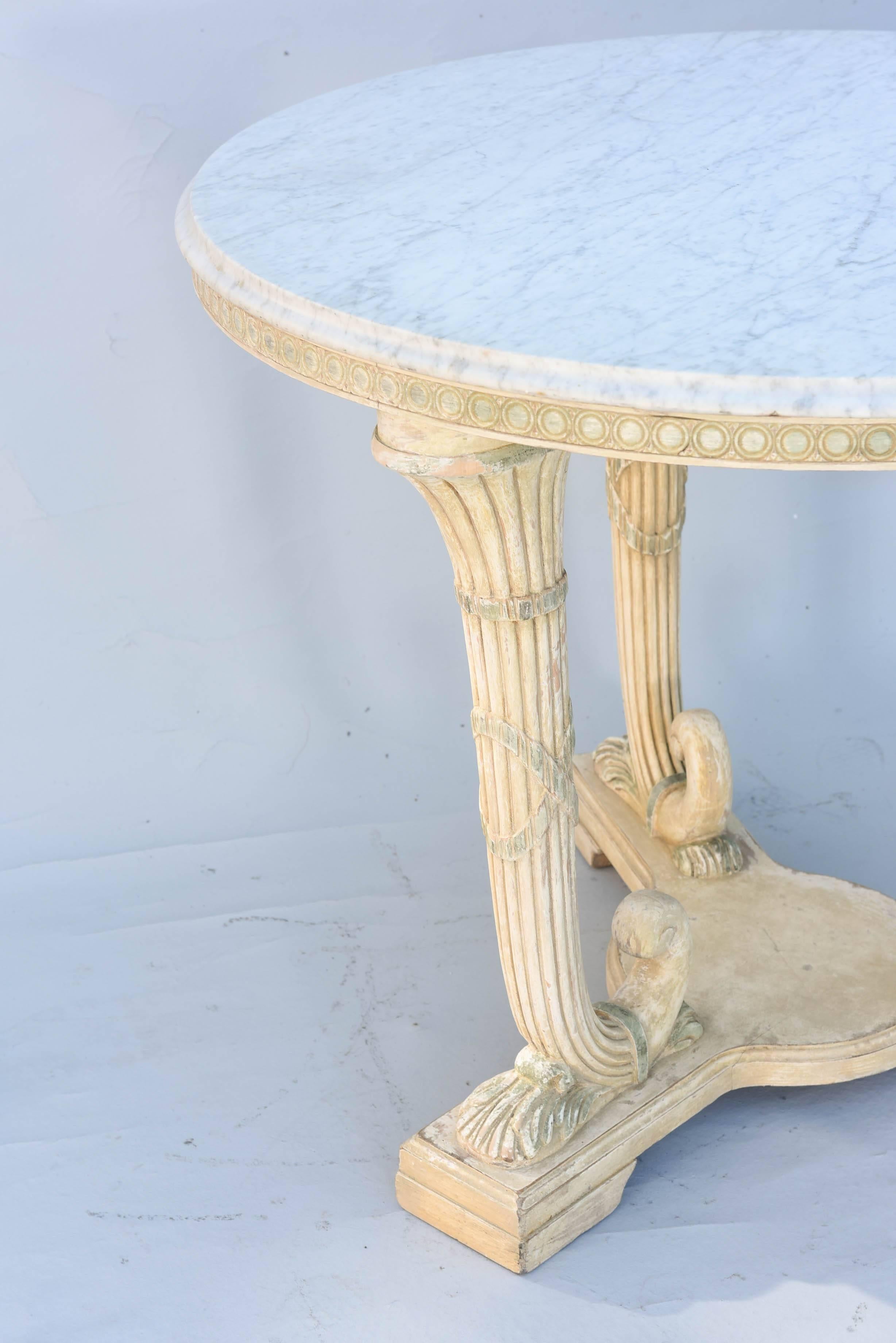Center table, having a round top of Carrara marble, on table base of painted wood, its guilloche carved apron over a trio of reeded horns, each wrapped with crossed ribbons, on tripartite base.  