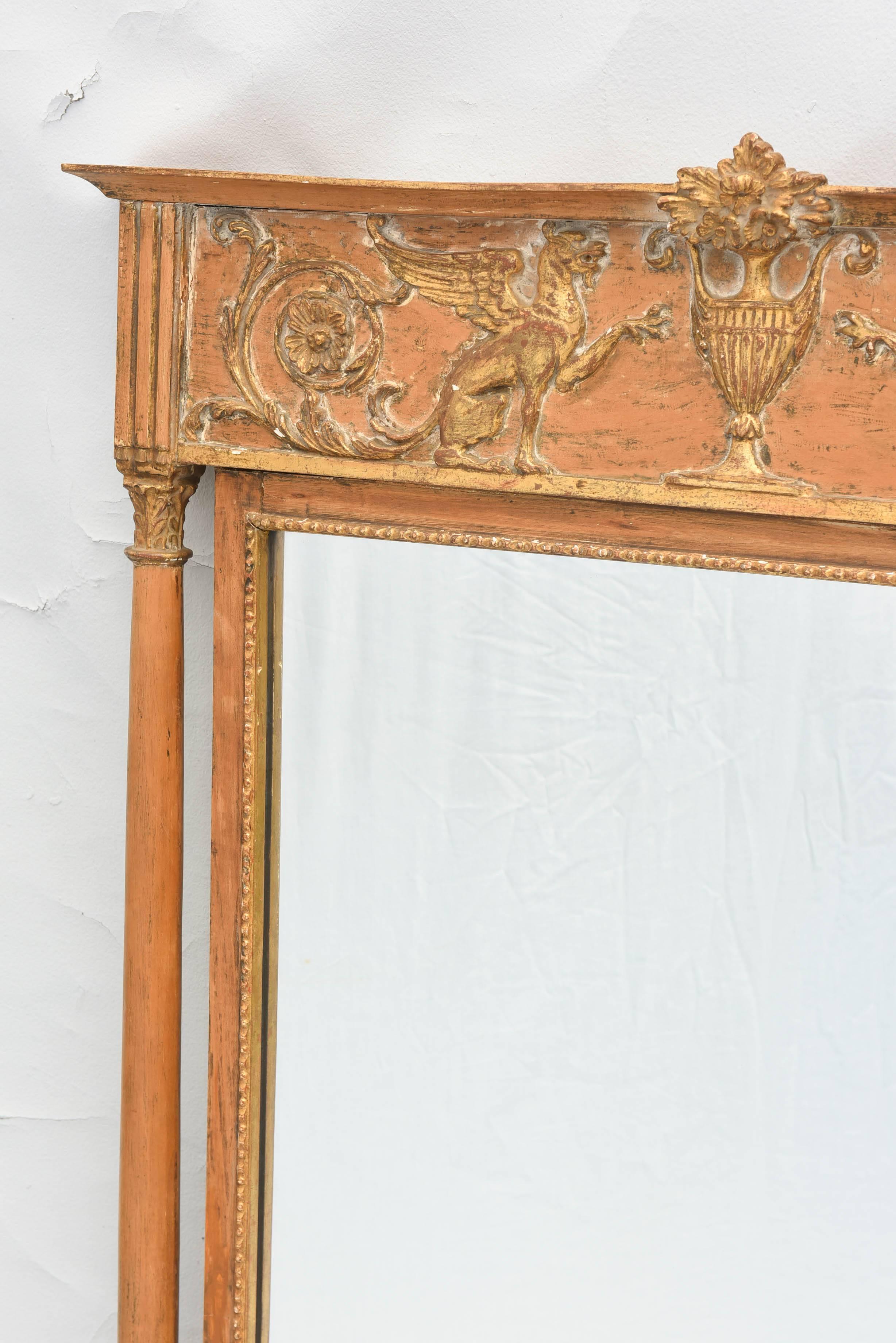 Pair of mirrors, in Empire style, having a molded cornice, over pediment, outcarved with flower-filled urn, flanked by Griffins and scrollwork, fluted stiles on round columns, ending in splayed feet. 

Stock ID: D8314