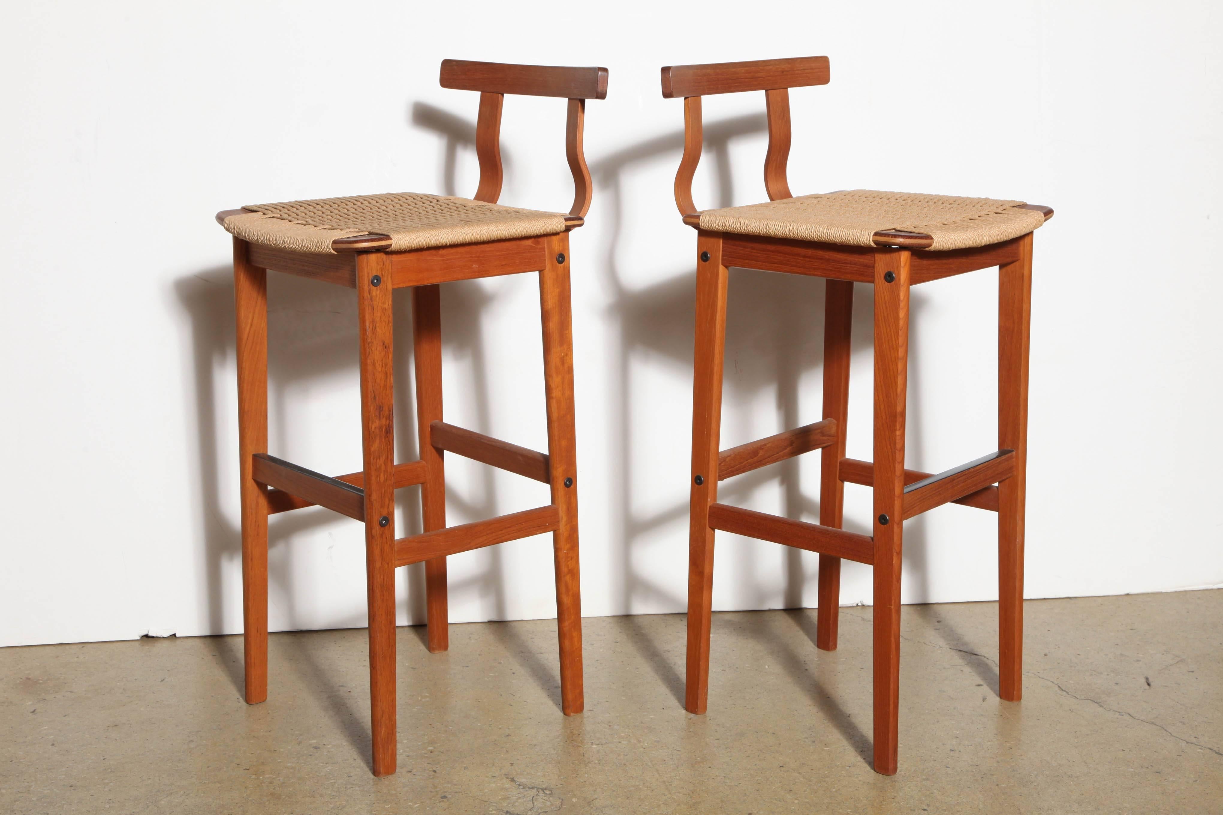 Pair of Scandinavian Modern teak and woven cord bar stools. Featuring an open rectangular teak framework with four supports, curved teak back support, woven heavy rope cord seat and footrest. Niels Otto Moller style, late 1960s. Natural. Neutral.