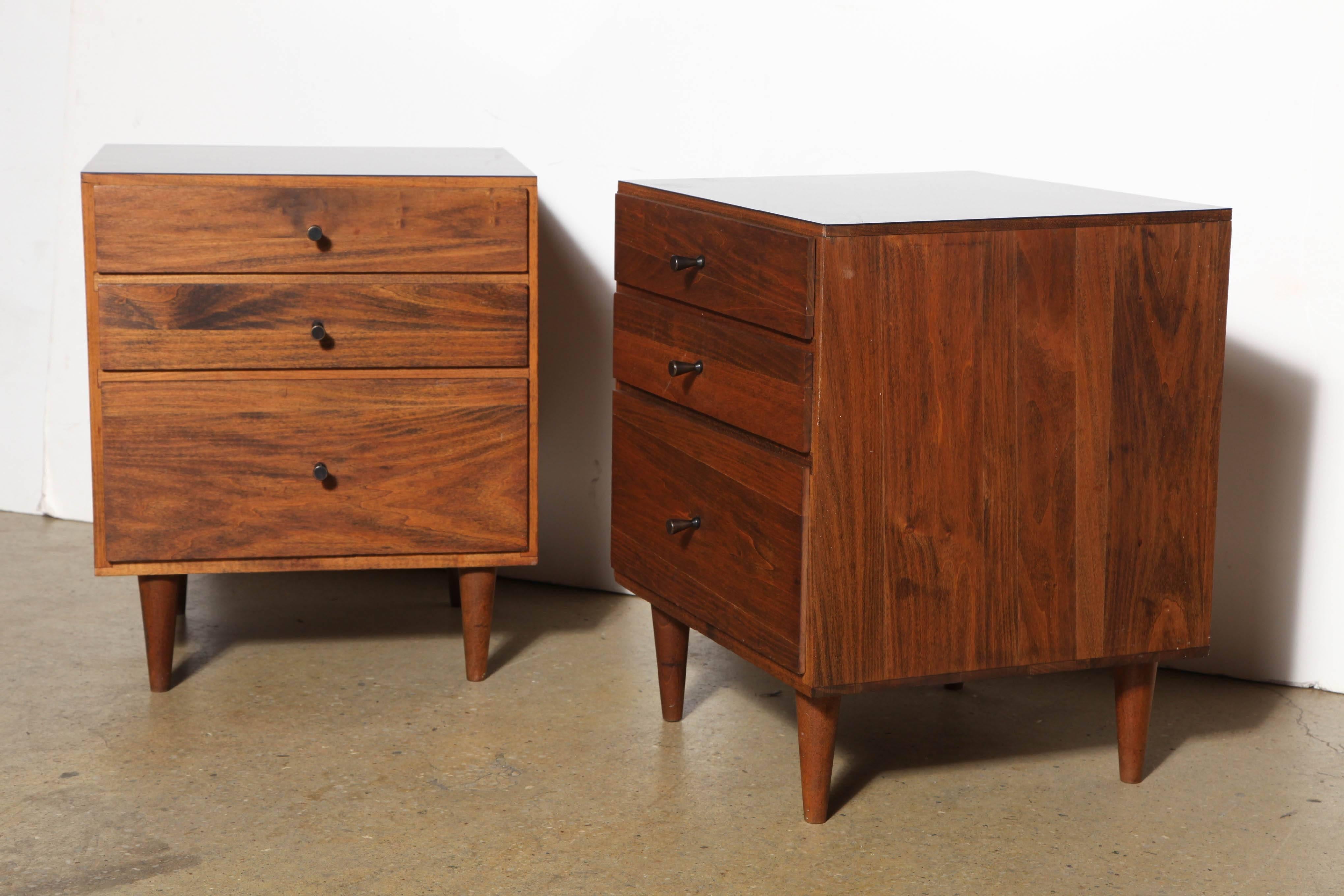 Pair of MId Century Paul McCobb Dark Black Walnut and Black Micarta Lower Bedside Tables. Solid. Compact. Heavy. Featuring a rectangular form in Black Walnut, three drawers, four (5.5H) dowel legs, Black Formica surface and classic McCobb conical