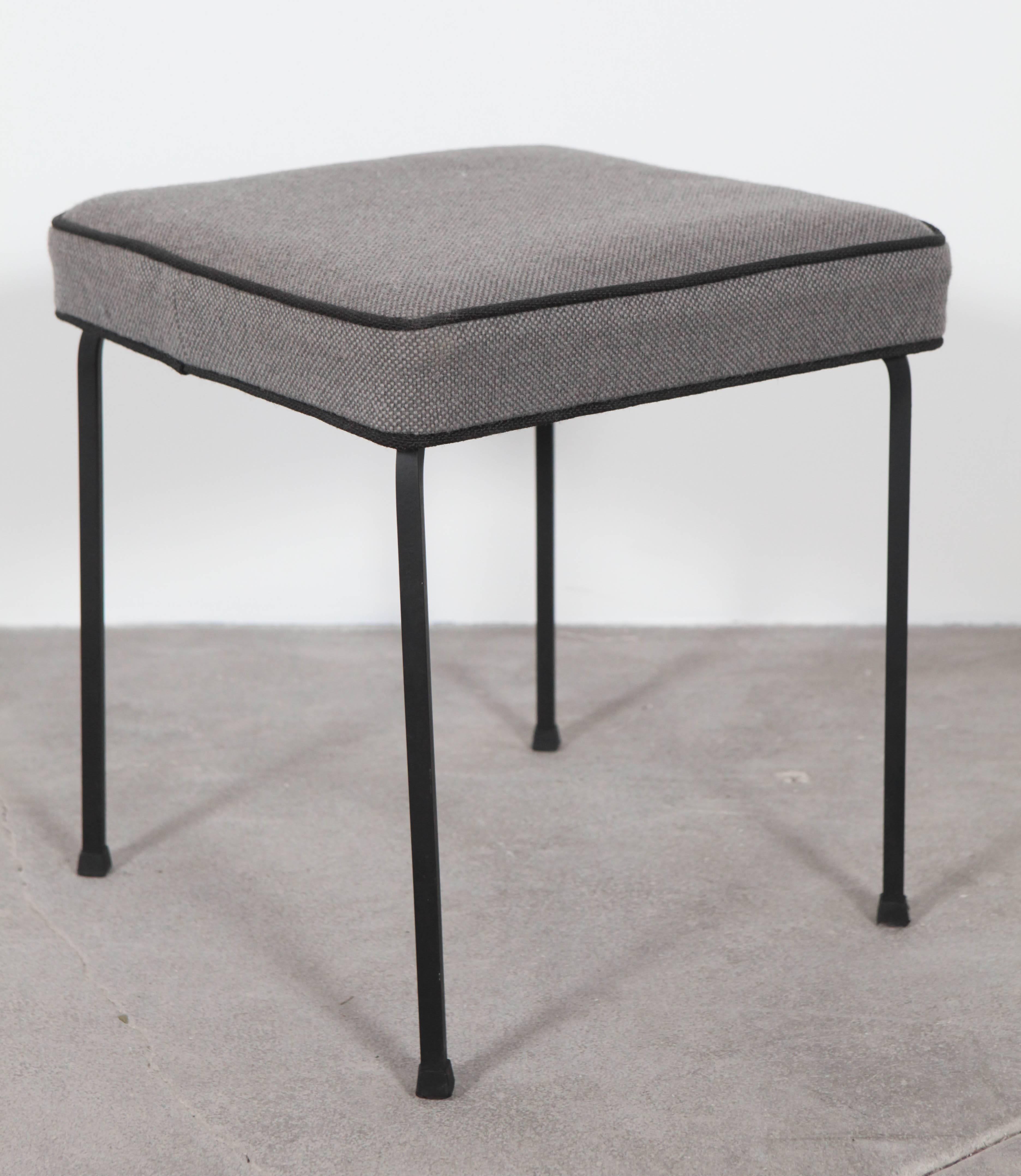 Low metal stools with upholstered grey top with black piping.