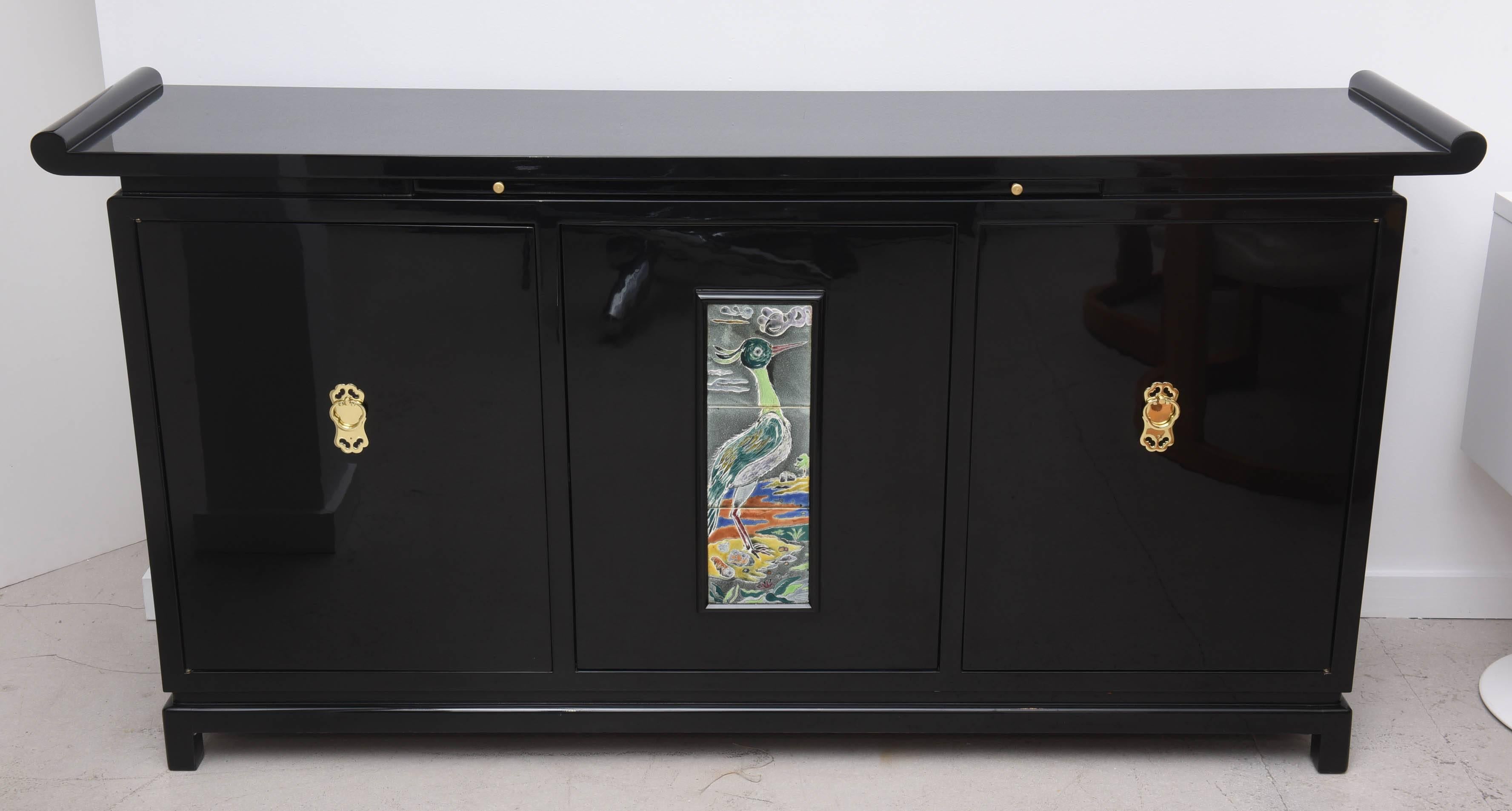 Mid-Century Modern credenza in the Asian Style with multi-color ceramic plaque. The plaque has a bird motif executed in a painterly fashion. The interior of the server maintains its original green color.