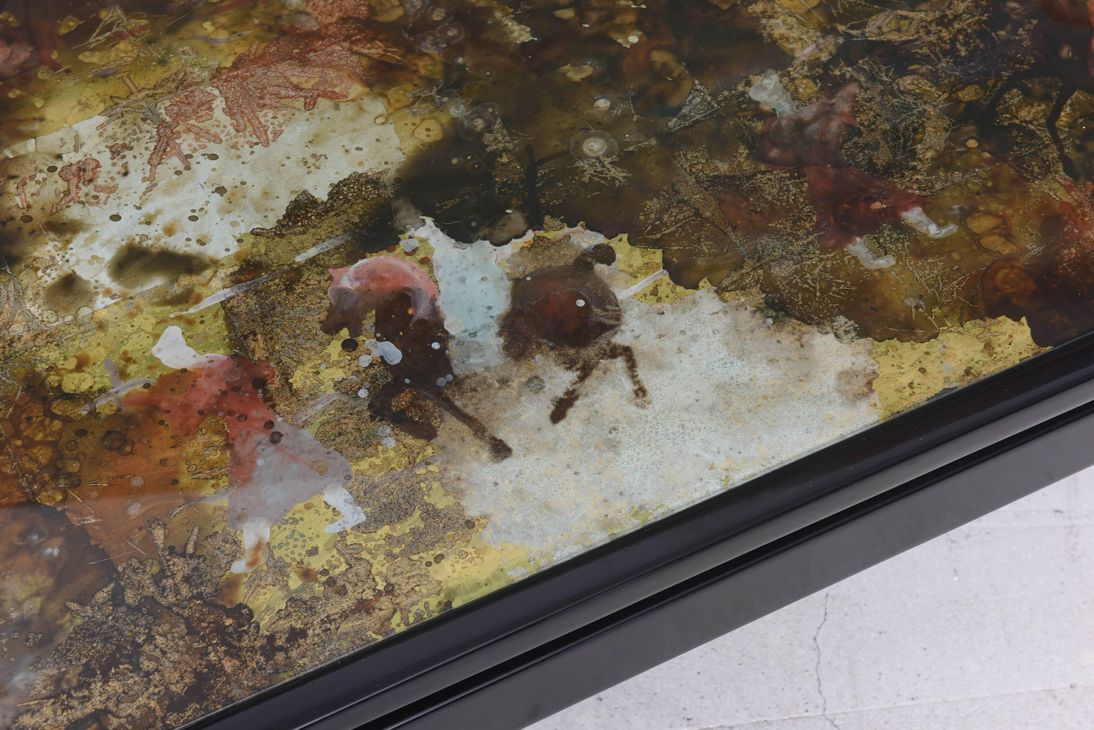 Vintage reverse painted glass coffee table with black lacquered base. The motif on the table top includes foliage and horse motif in an atmospheric moody palette.