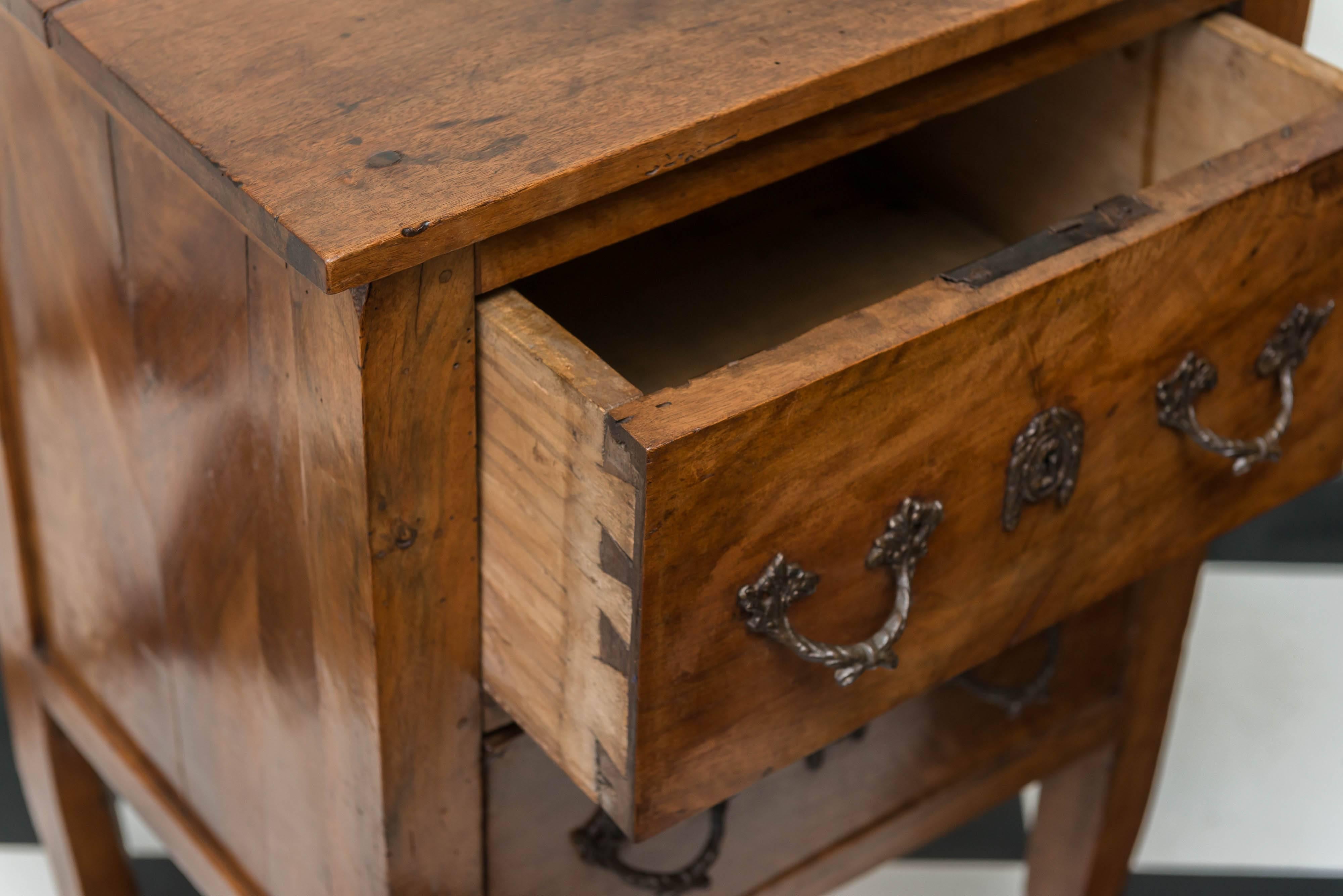 18th century Italian neoclassic walnut comodino with two drawers. Bookmatched boards on the top and sides. All solid woods, no veneers. Panel and framed sides with pegged construction overall. Subtle curve to the tapered legs. Older brass pulls and