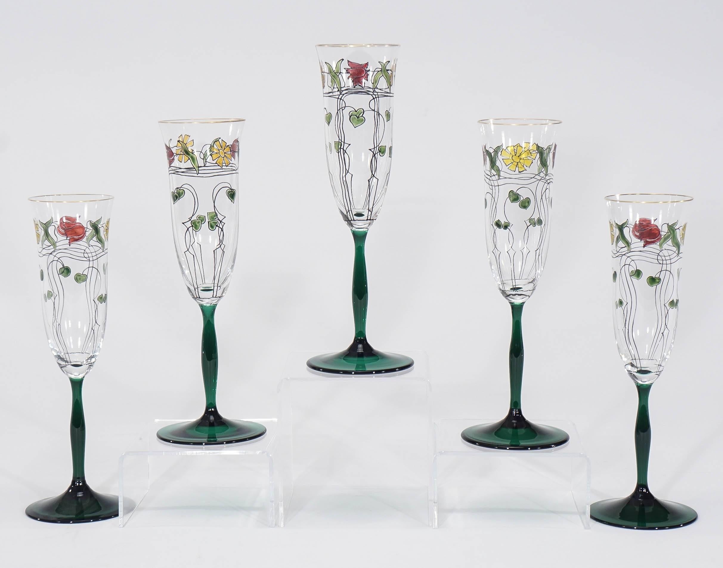 This rare and impressive set of ten tall champagne flutes features clear bowls and emerald green drawn stems which suggest a tulip. The hand-painted poly-chrome floral enamel decoration is beautifully articulated in an Arts and Crafts motif adding