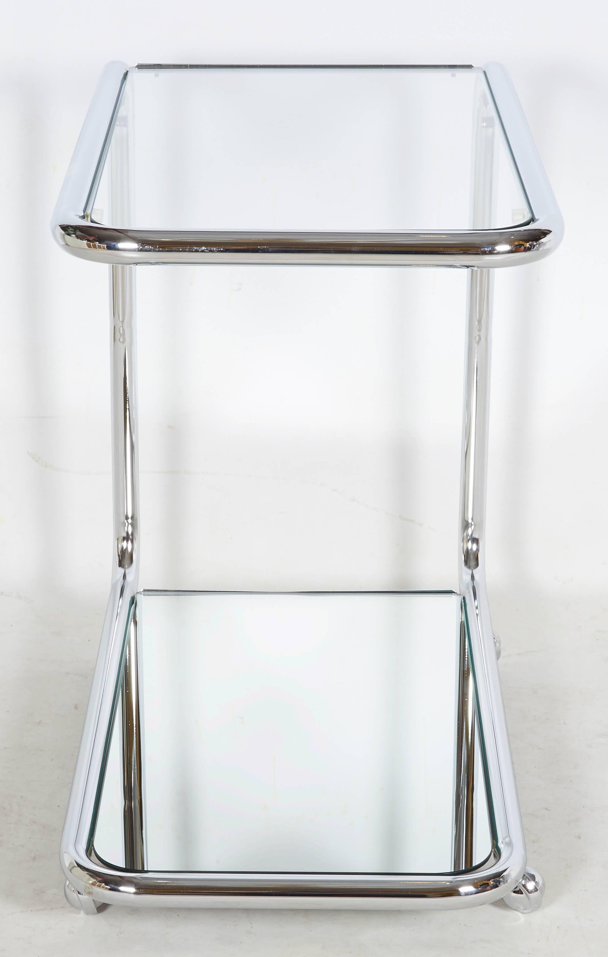 Lovely Bauhaus style bar or serving cart from the Art Deco revival period of the 1970s. The sinuous cart holds a clear glass top and a mirrored glass bottom. Please contact for location. Offered by Las Venus by Kenneth Clark, New York City.