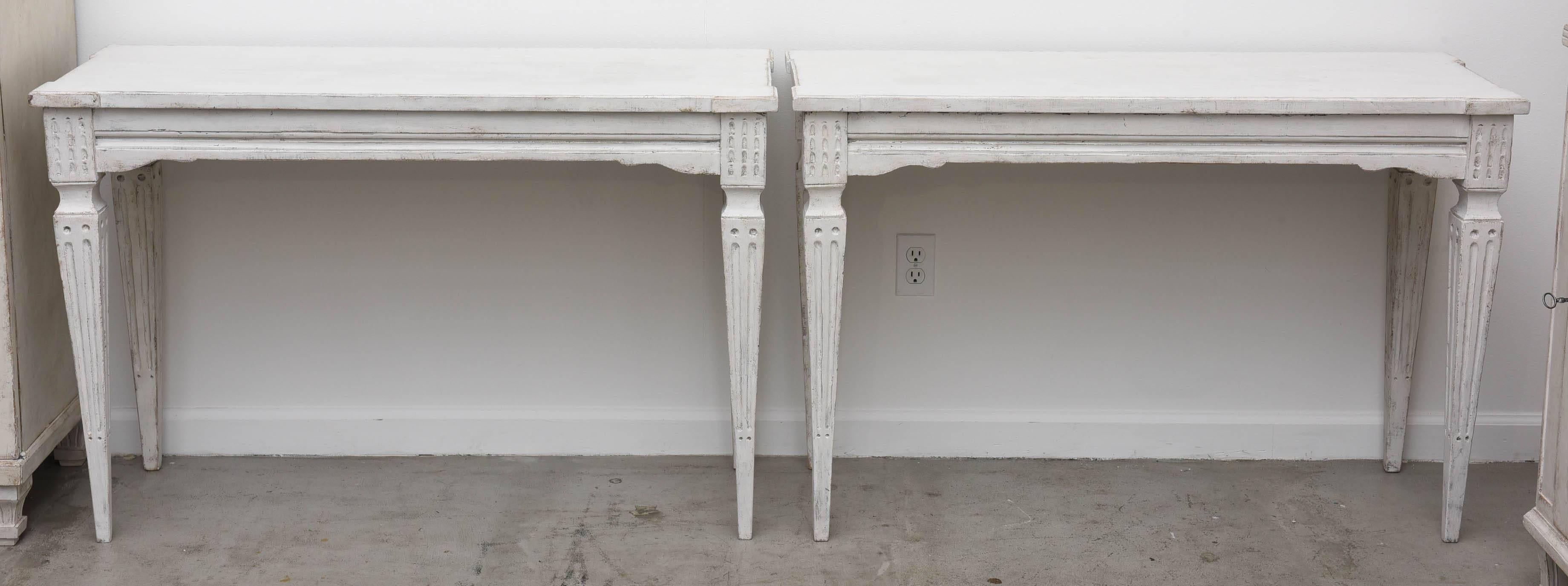 Pair of antique Swedish console tables. Classic Scandinavian design, simple carvings on the corners, square tapered and fluted legs. Gustation grayish white
distressed finish.  There are Swedish blue highlights in the carved detailed area.

Circa
