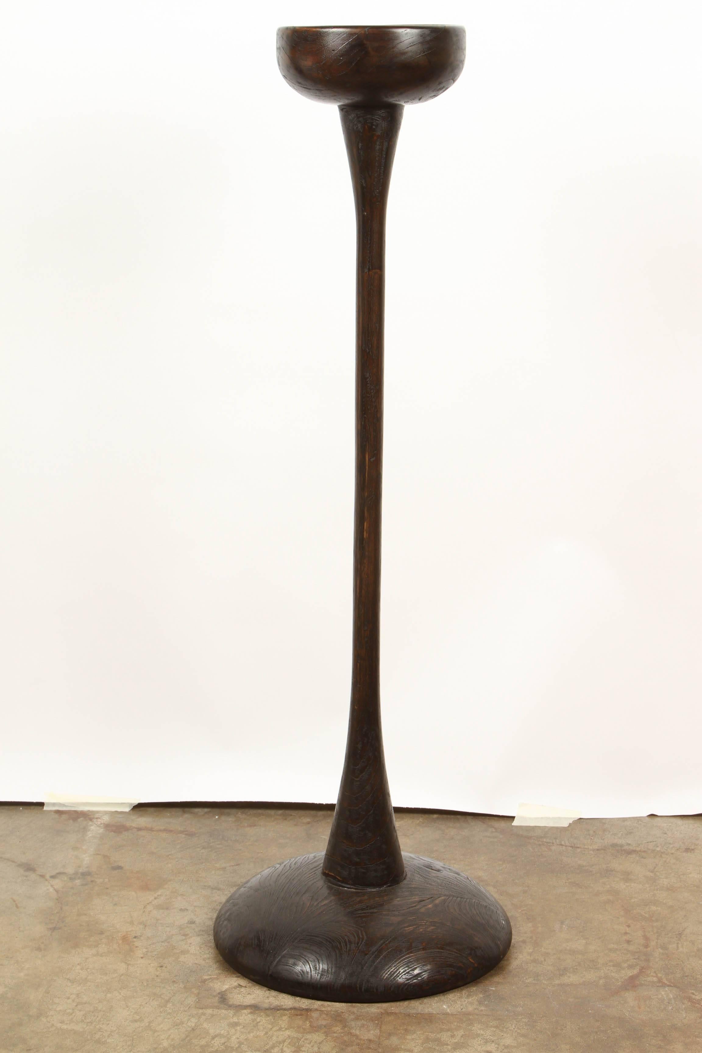 A pair of tall (46 1/2 inches) solid teak central Java plant stands, each with a deep black patina. The base upon which the plant sits rises from a graceful pillar that in turn rises from a rounded base. A plant that grows straight up would be