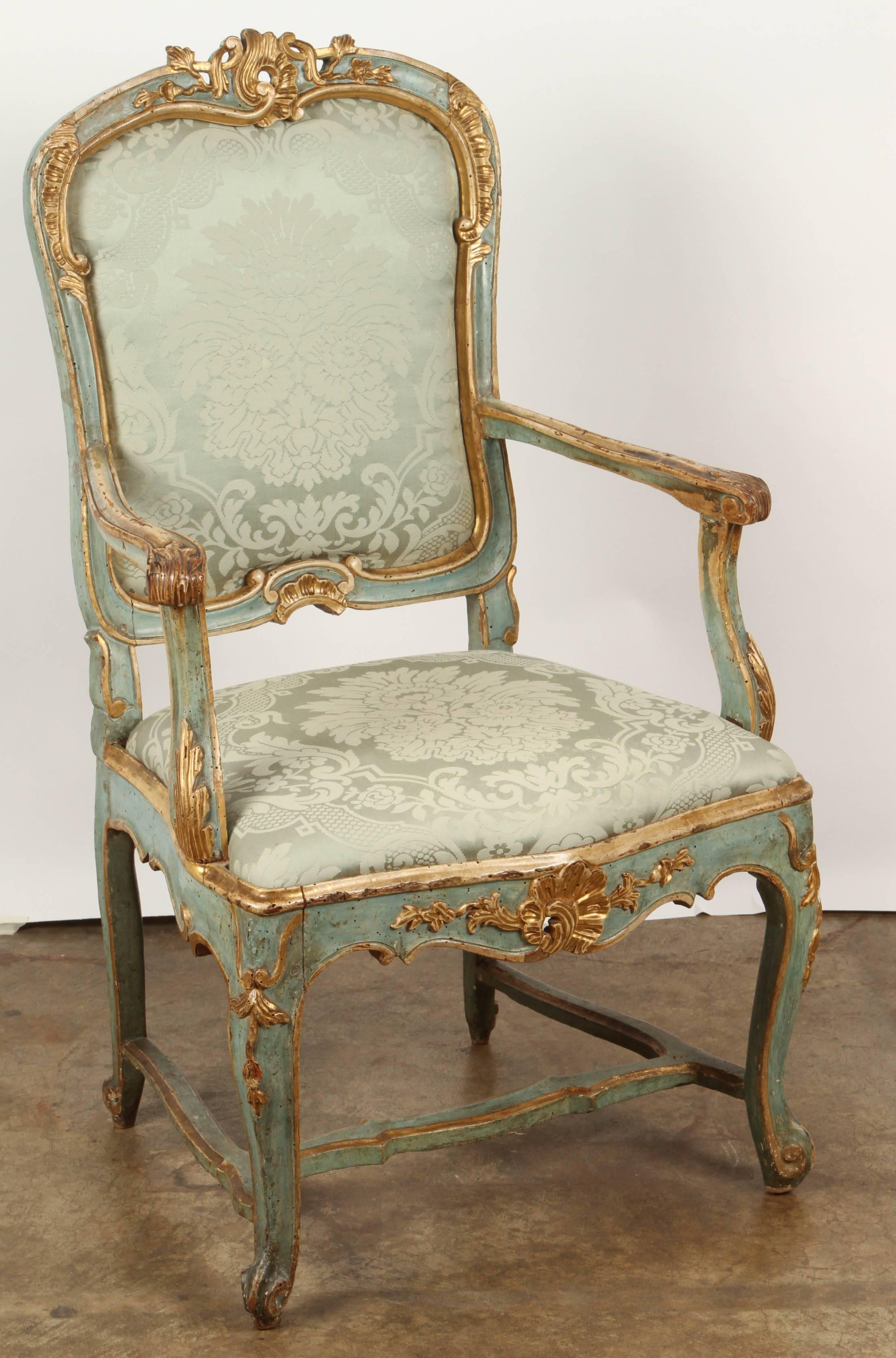 The chair, upholstered with matching silk damask to the seat and back rest, the slightly rounded crestrail decorated with a central rocaille and flower heads, the ears decorated with rocaille, the shaped arm rests ending in carved acanthus leaves.
