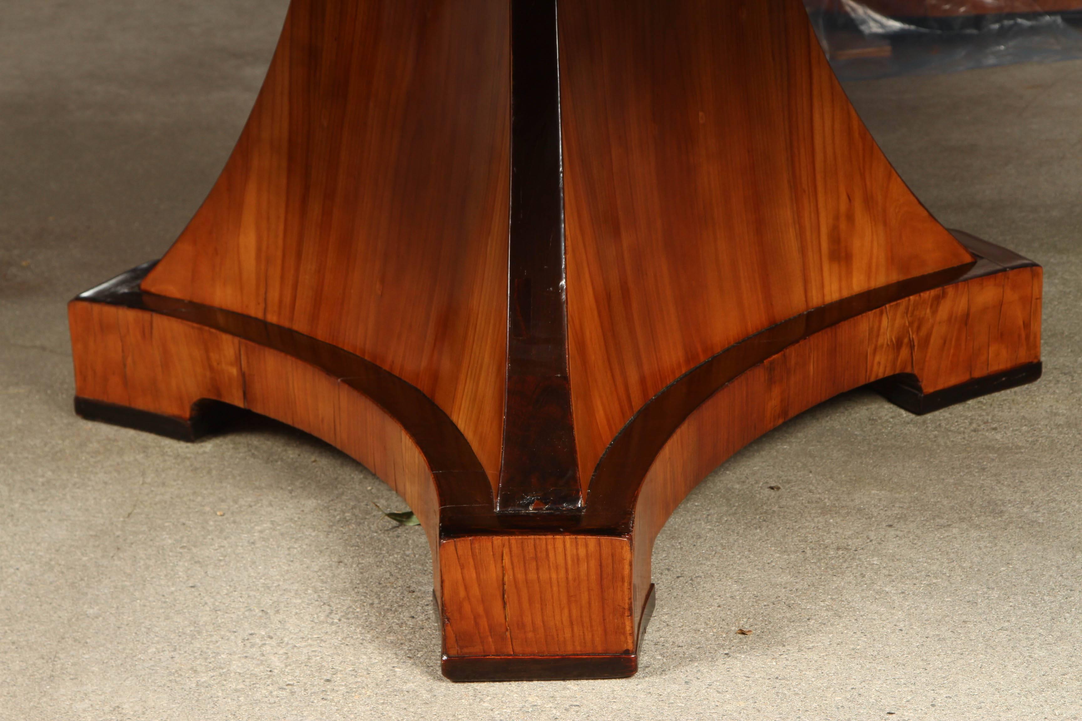 A round Biedermeier table, with a large group top on a tripartite base, with an elm veneer and ebonized trim detailing. This style of furniture, such as this lovely table, was meant to  bring both elegance and utility to owners' private lives. 