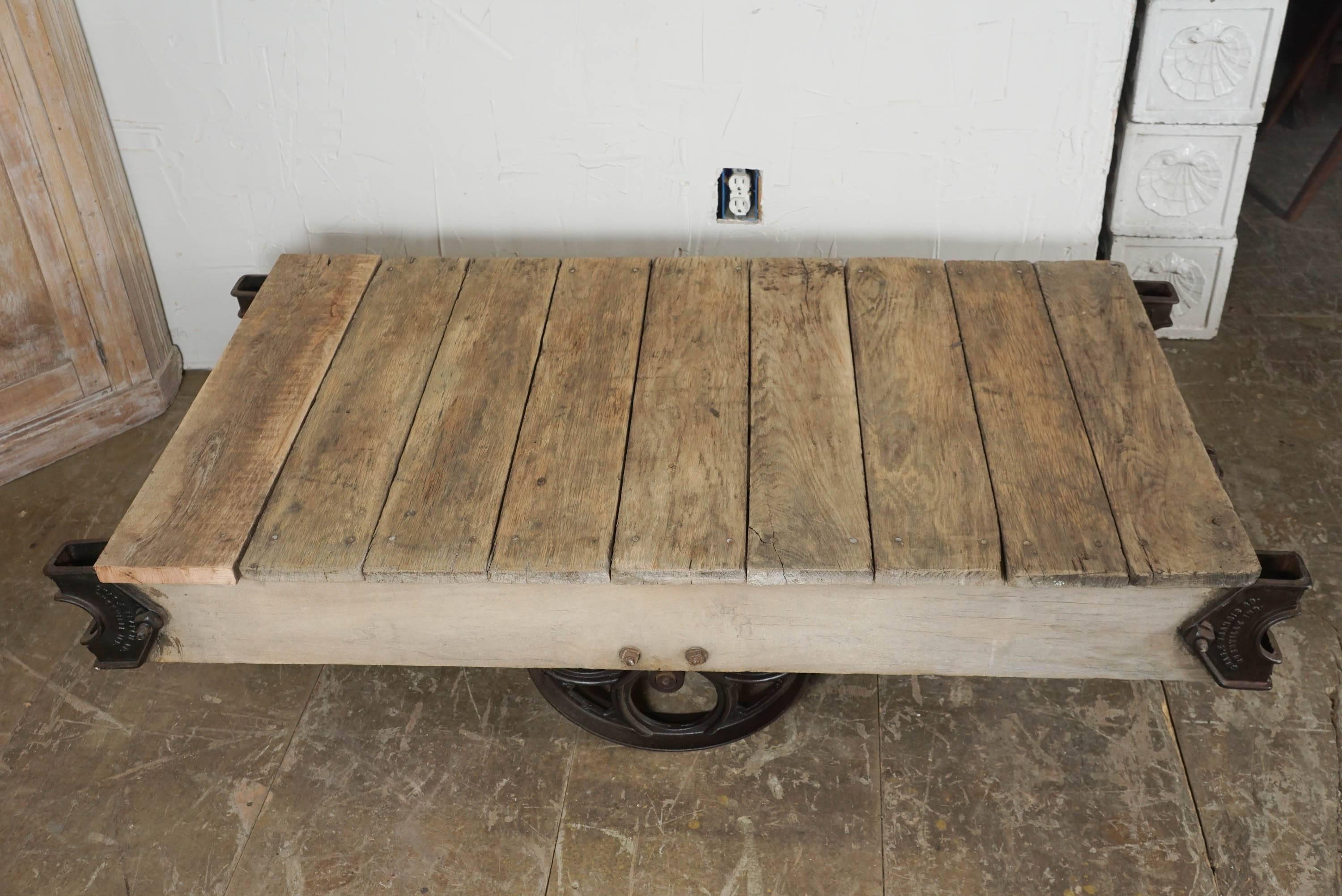 Vintage industrial rustic rolling cart made of wood planks and cast iron wheels and brackets, the loader has two end wheels that swivel and are slightly shorter than the larger sides ones for easier movability.  Cart does sit flat on the ground but
