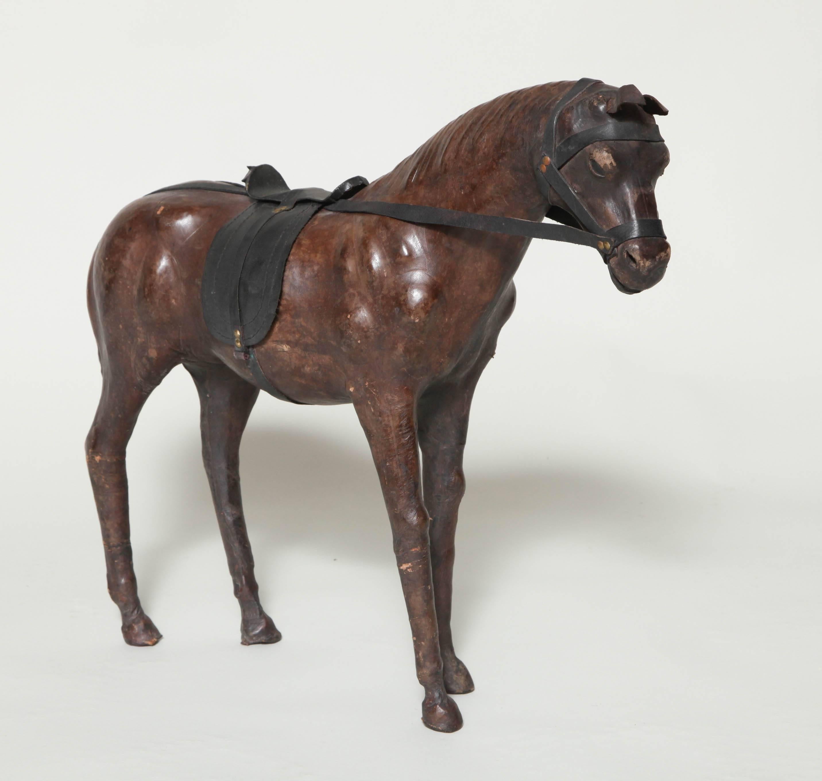 Charming and very decorative leather standing horse, the body (wood - papier mâché?) covered in thin and richly tanned leather, having inset glass eyes and brass studded tack.